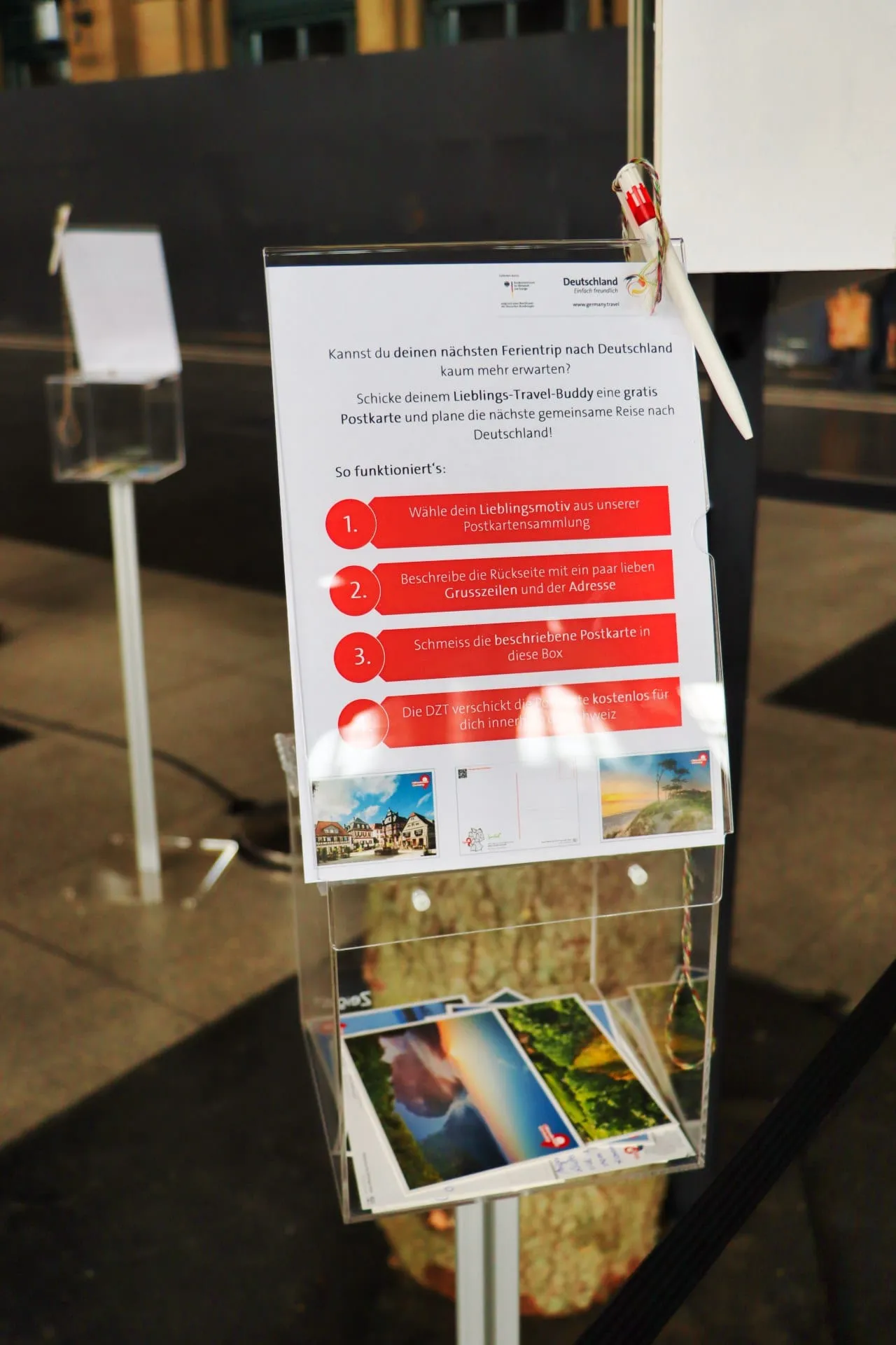 Acrylbox mit Anleitung «Schicke deinem Lieblings-Travel-Buddy eine gratis Postkarte» und eingeworfenen Postkarten