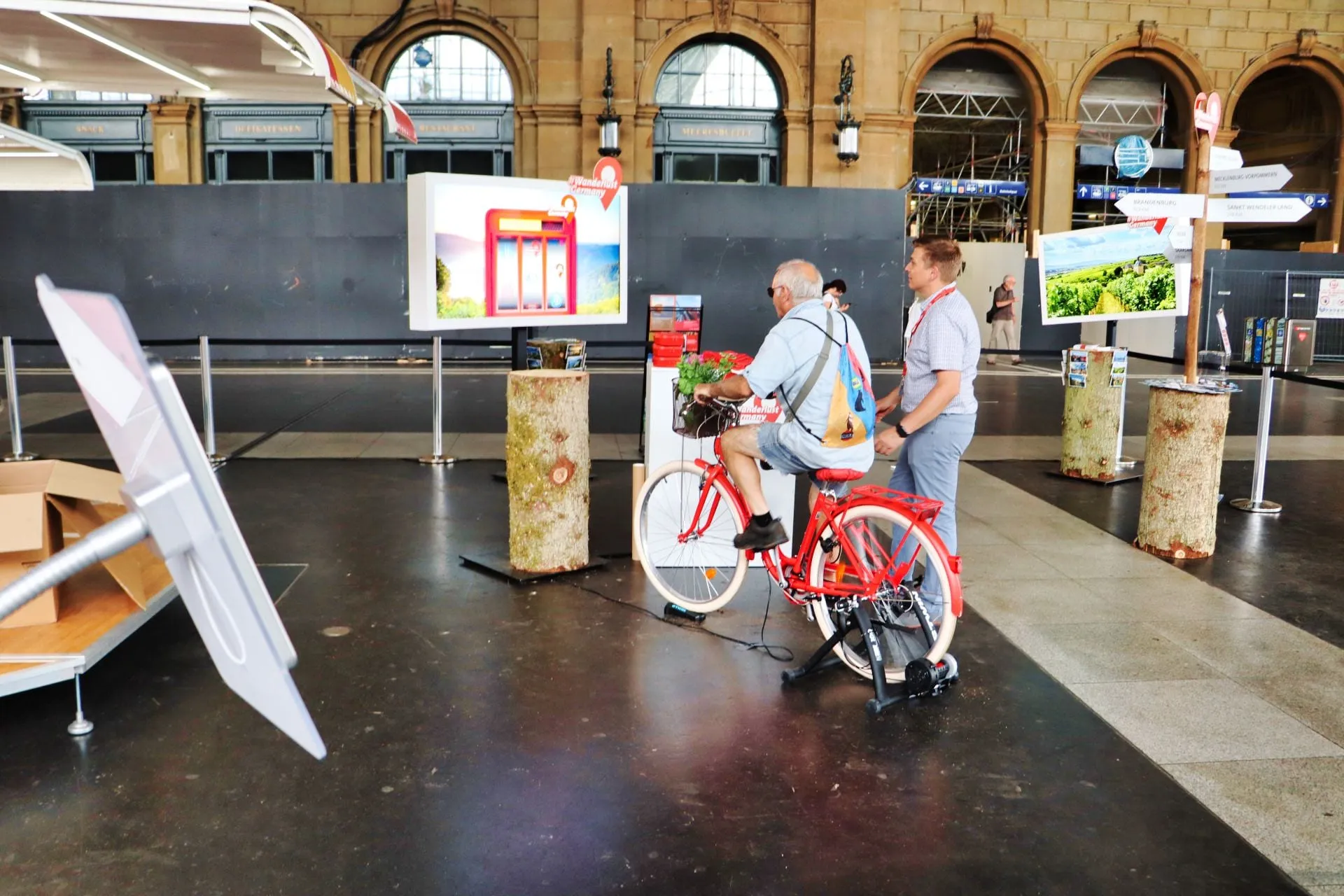 Mann fährt auf dem roten Velo auf der Rolle vor dem Bildschirm des Velo-Games, Promotor daneben