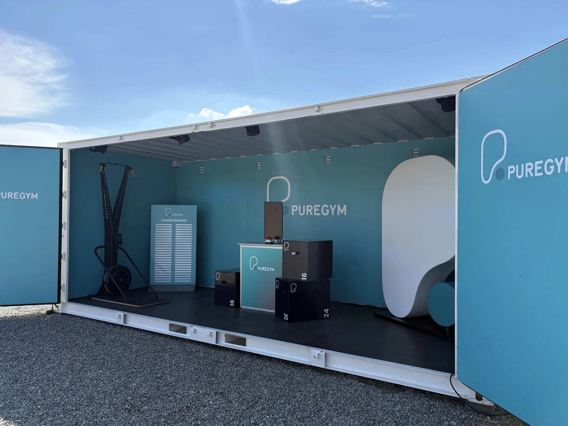 White container with its long side open, turquoise PureGym interior, ski ergometer, leaderboard, plyometric boxes and a white logo sculpture