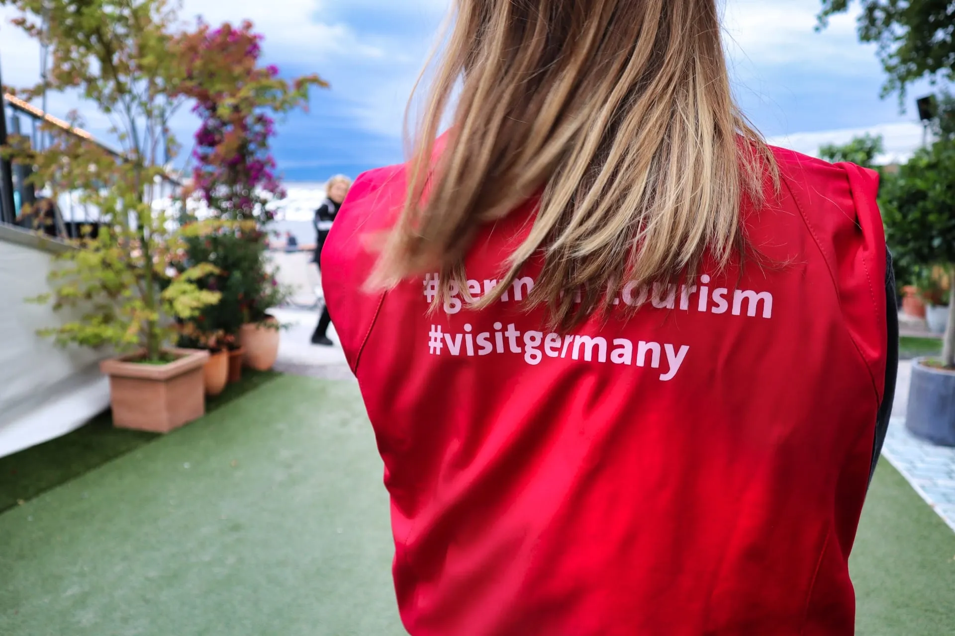 Rückenansicht einer Standmitarbeiterin in roter Weste mit Aufdruck #germantourism #visitgermany