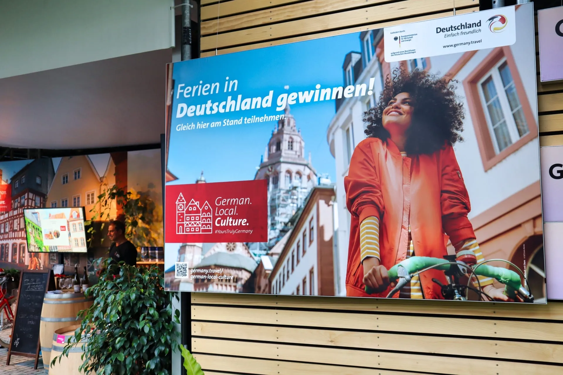 Plakat «Ferien in Deutschland gewinnen» mit Frau auf Velo an der Holzlattenwand des Stands