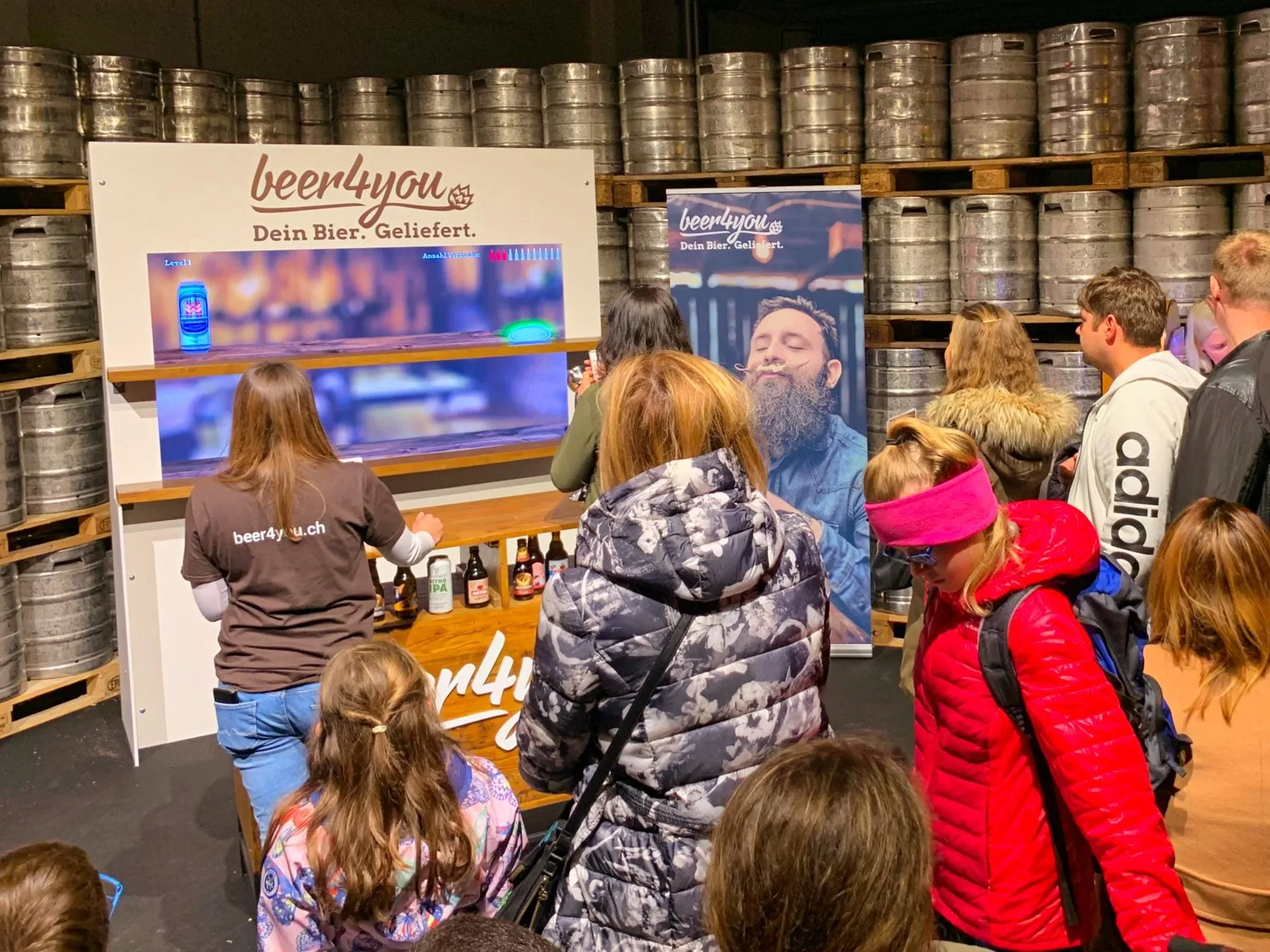 Besuchende spielen das beer4you-Game an der Holzbar, umgeben von gestapelten Bierfässern