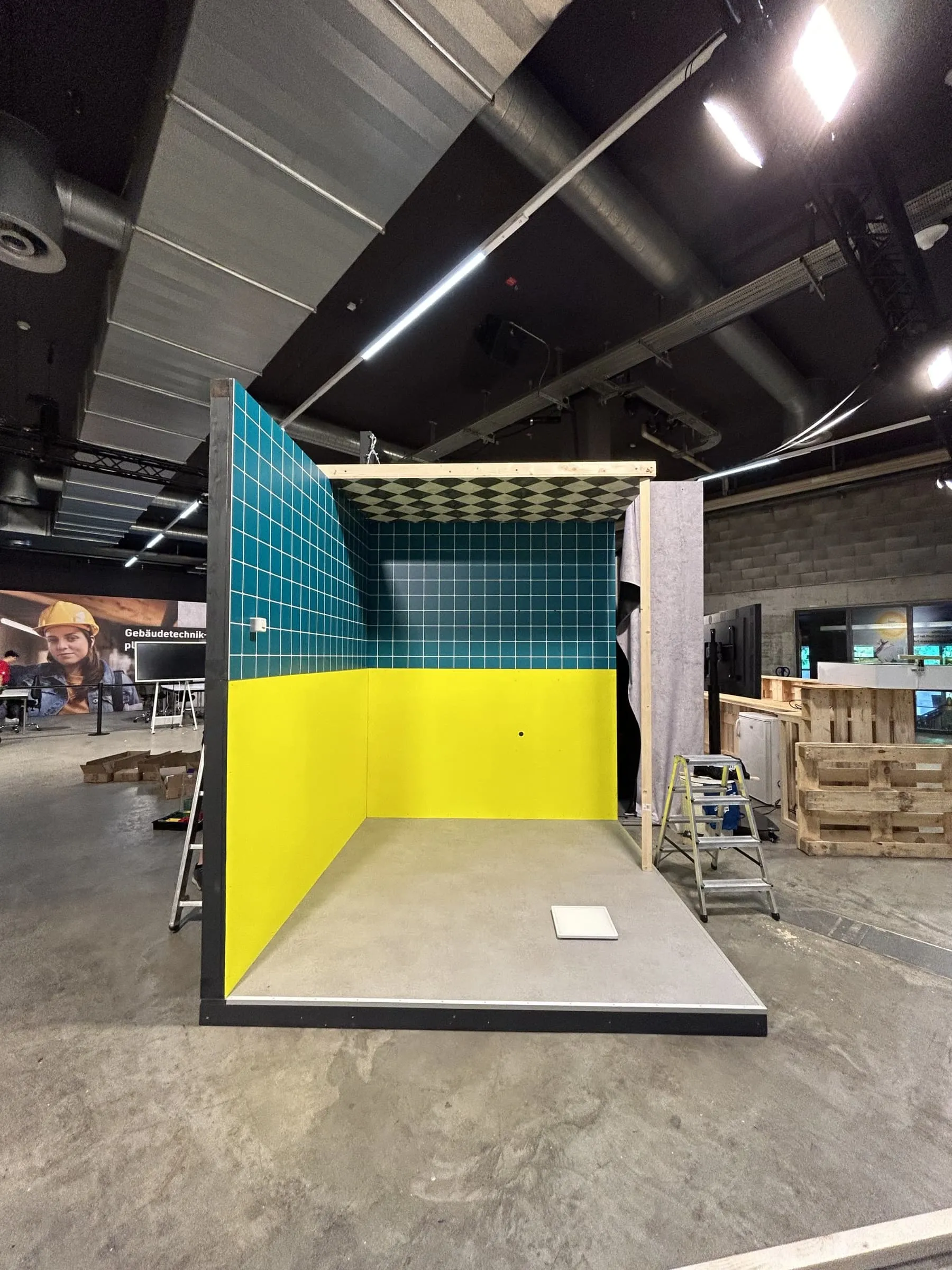 Kubus mit blauen Plättli, gelben Wänden und Schachbrettdecke in der Messehalle, noch ohne Einrichtung