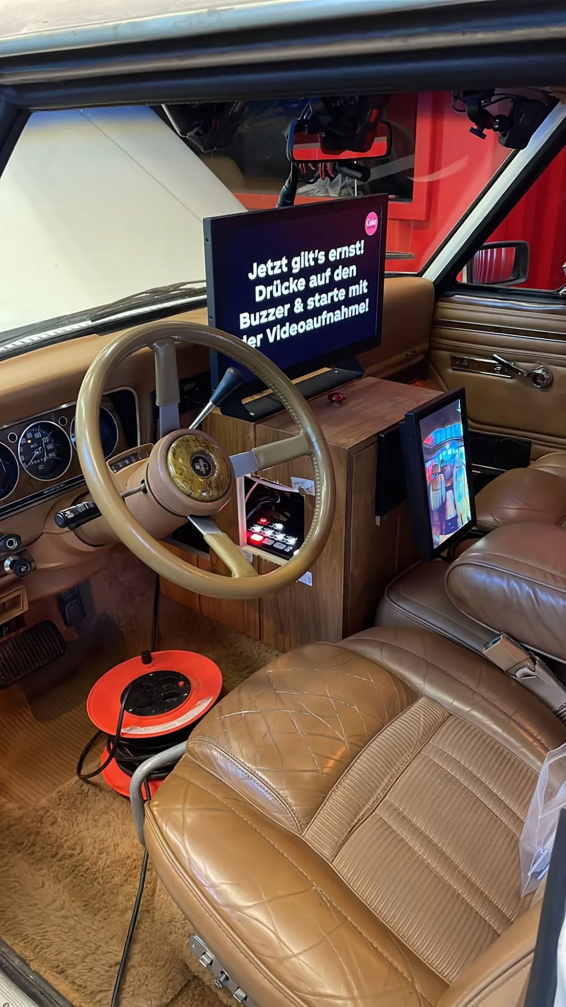 Karaoke-Bildschirm mit Anleitung «Drücke auf den Buzzer» und roter Buzzer im Cockpit des Jeeps