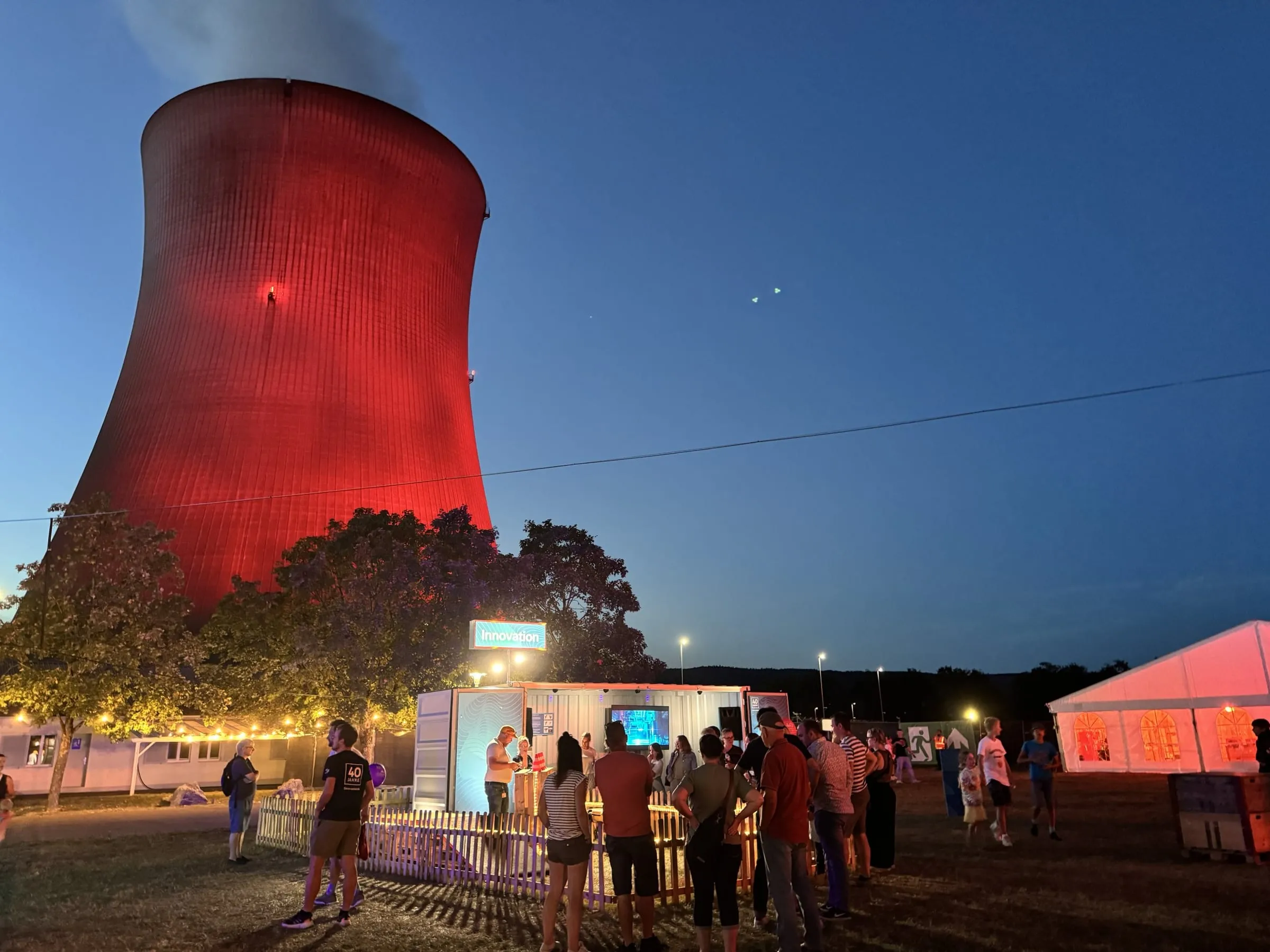 Rot angestrahlter Kühlturm bei Nacht über dem Innovation-Container mit Besuchergruppe