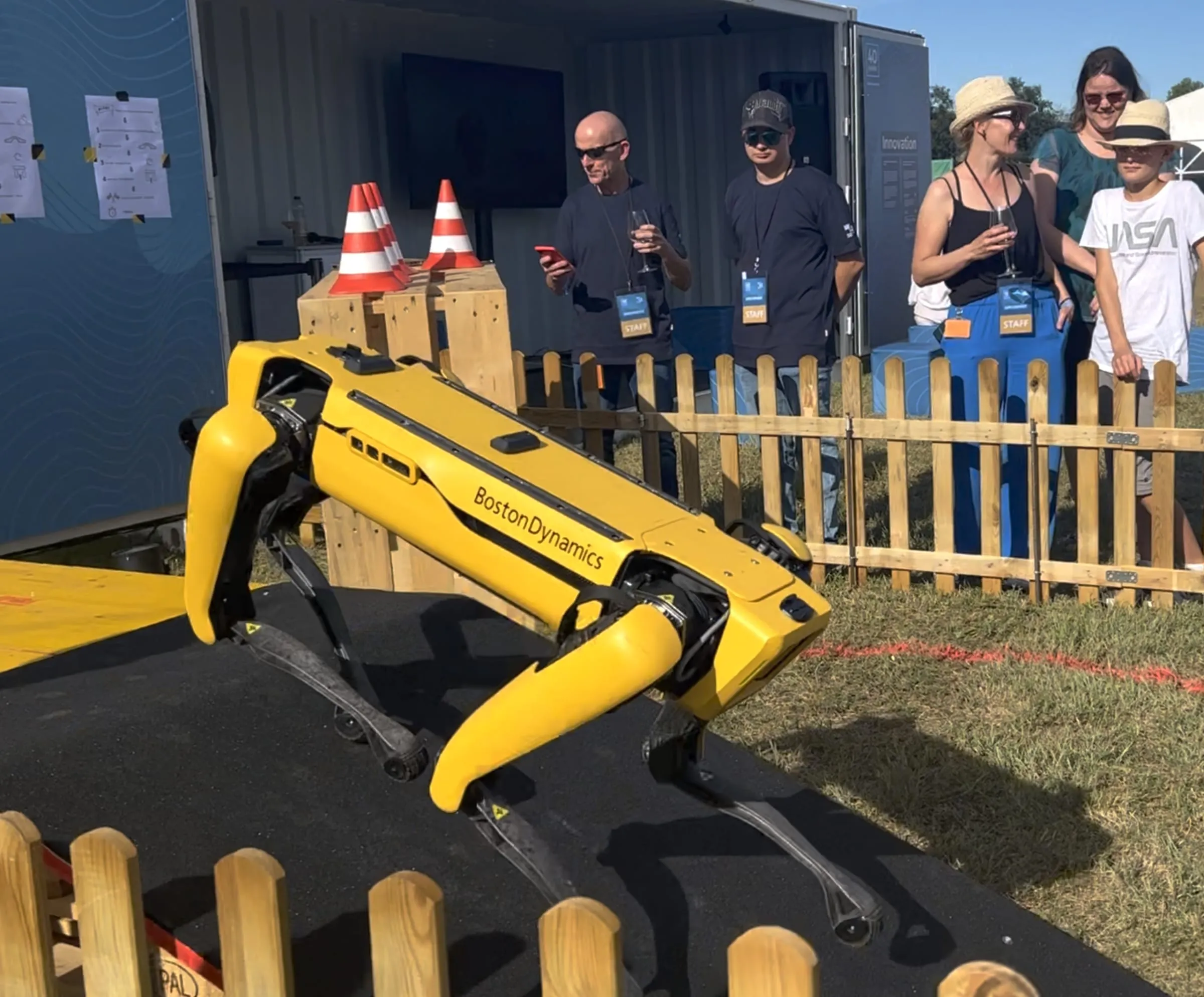 Gelber Roboterhund von Boston Dynamics auf einer Rampe, Zuschauende hinter dem Holzzaun