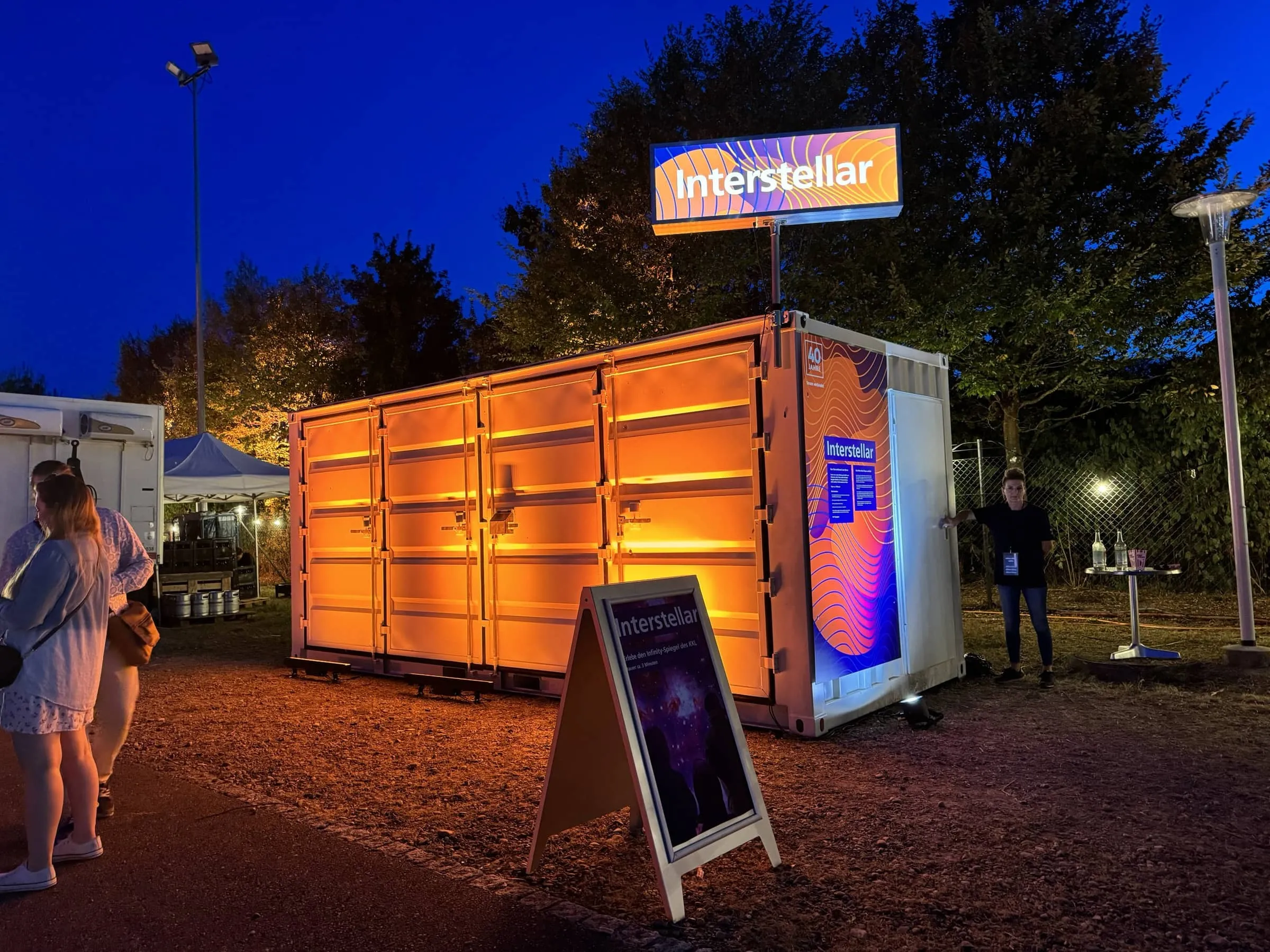 Orange beleuchteter Container mit Leuchtschild Interstellar und Aufsteller in der Abenddämmerung