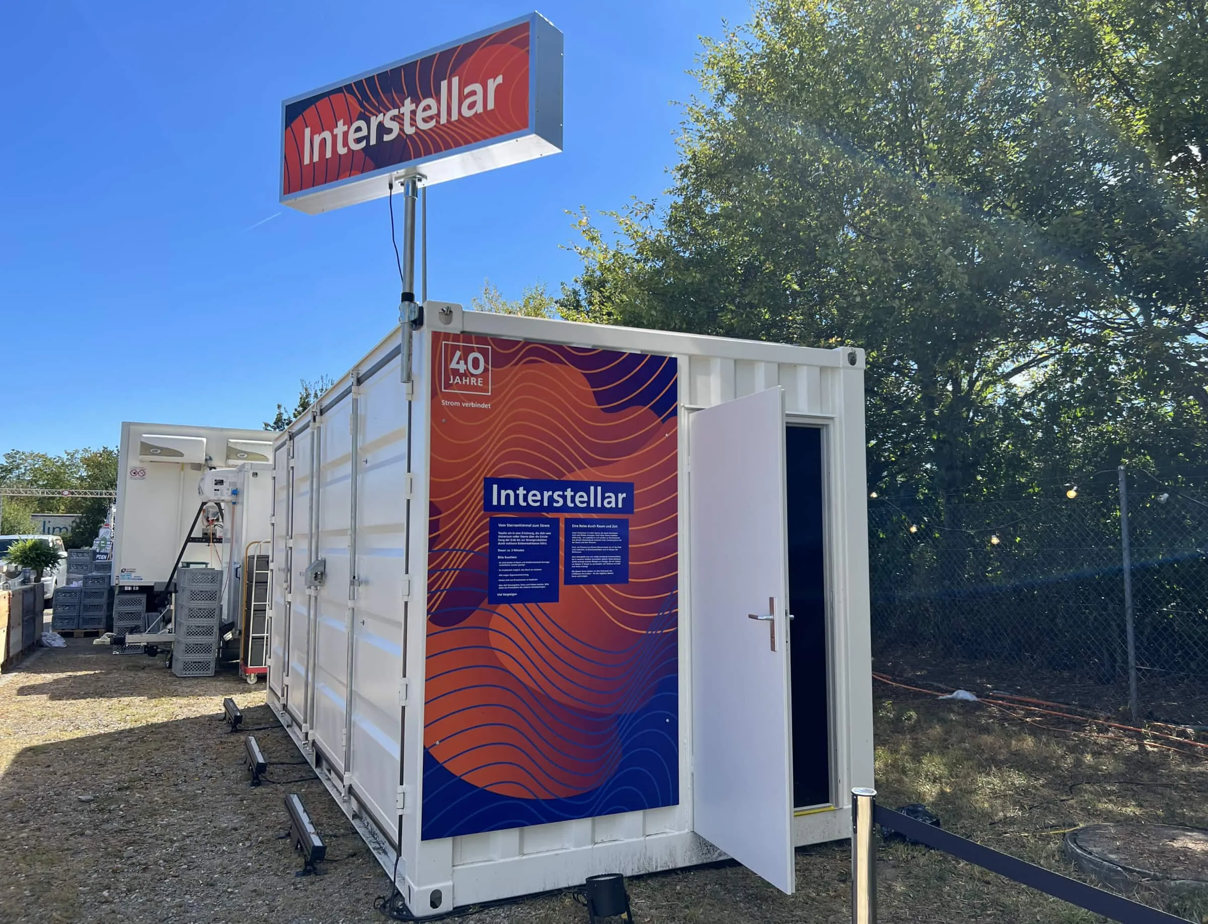 Weisser Container mit offener Türe, orange-blauer Interstellar-Grafik und 40-Jahre-Logo bei Tag