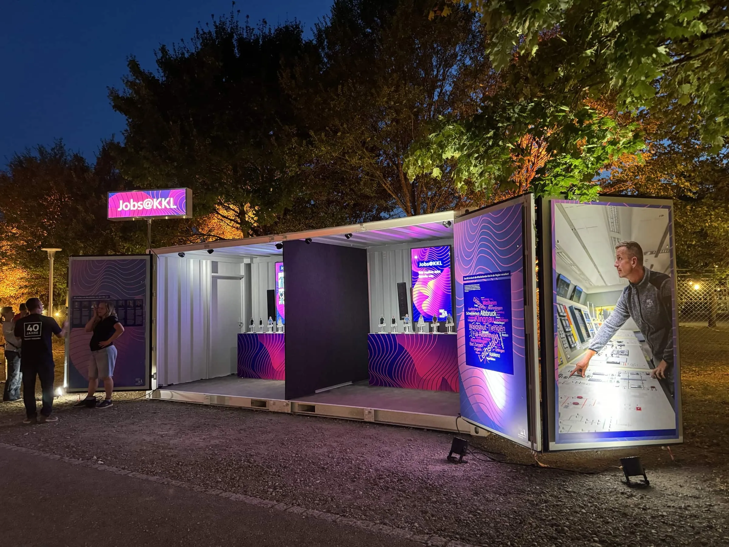 Violett beleuchteter Jobs@KKL-Container am Abend mit Foto eines Mitarbeiters im Kontrollraum auf der Türe