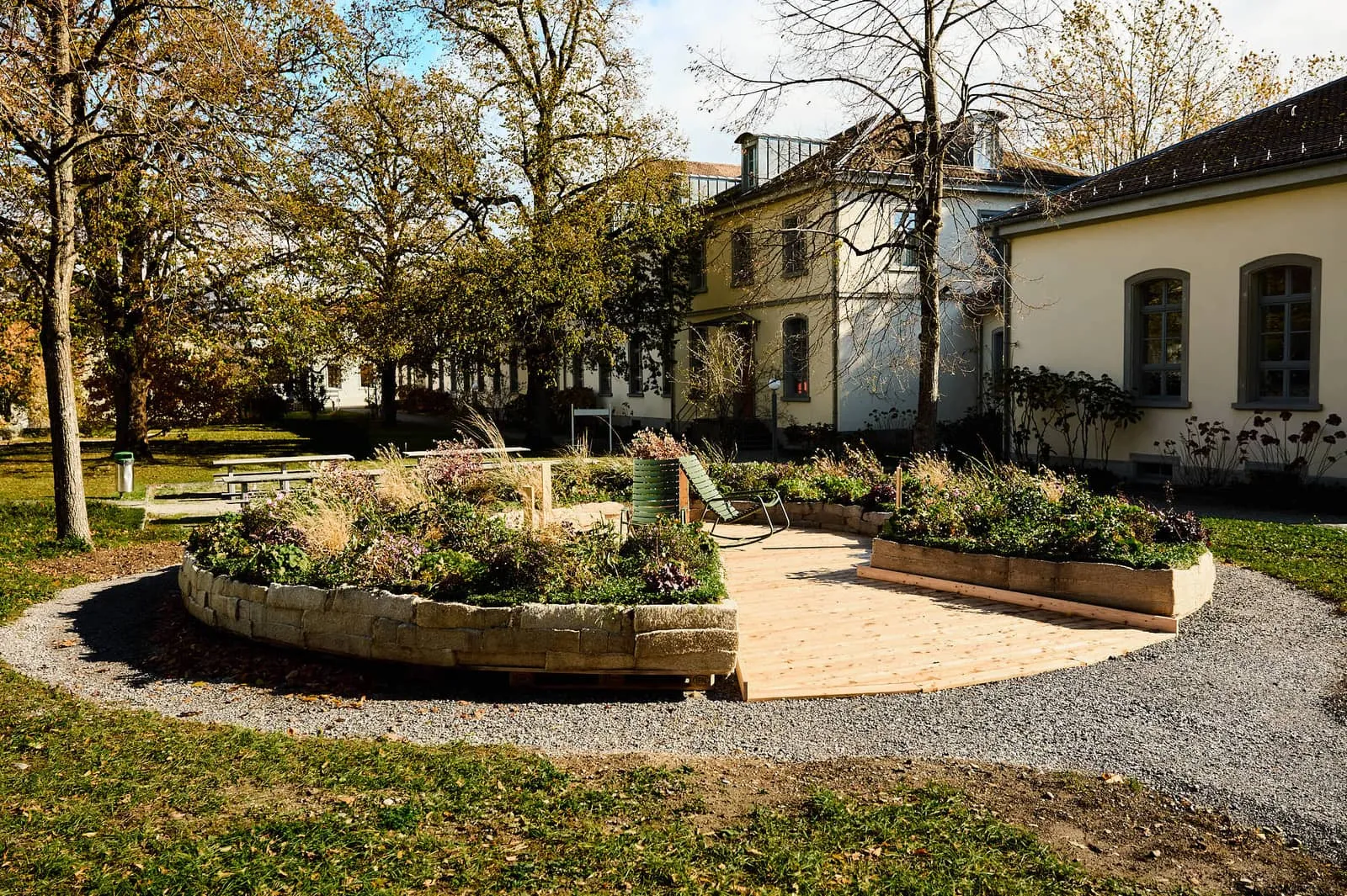 Completed flower ring with planted hemp-mat edging, a wooden deck and green rocking chair in a park outside clinic buildings