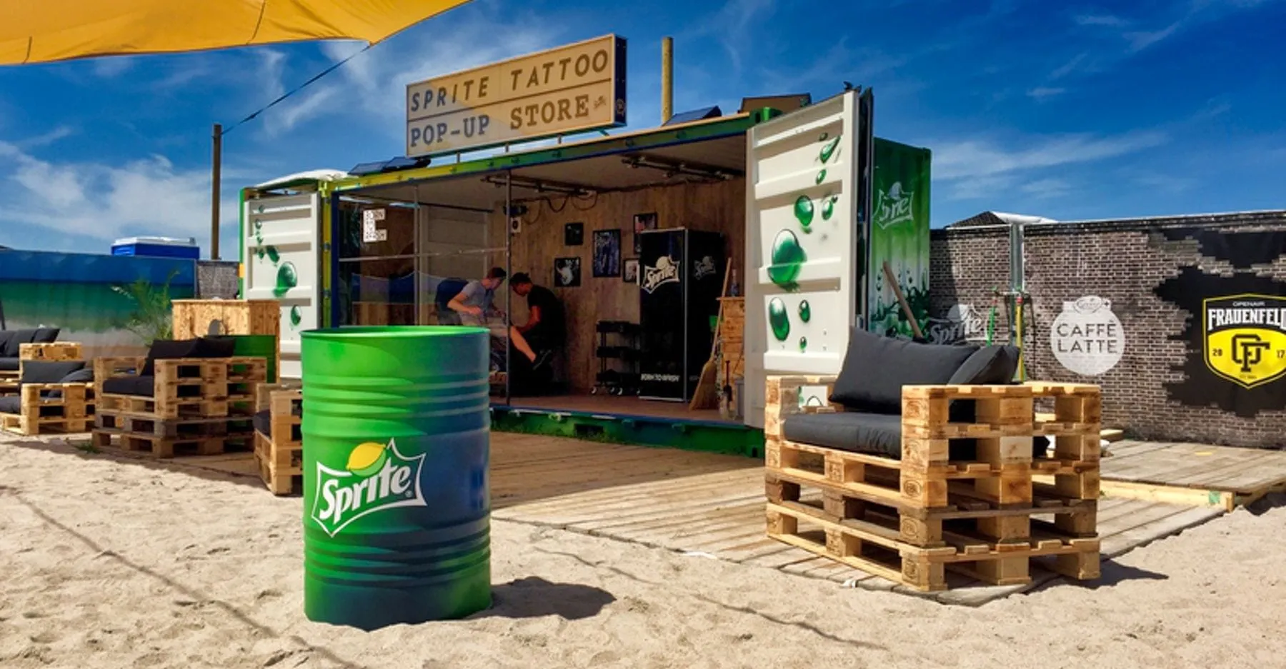 Sprite Tattoo pop-up store in a container standing on sand, with pallet furniture and a green Sprite barrel in front