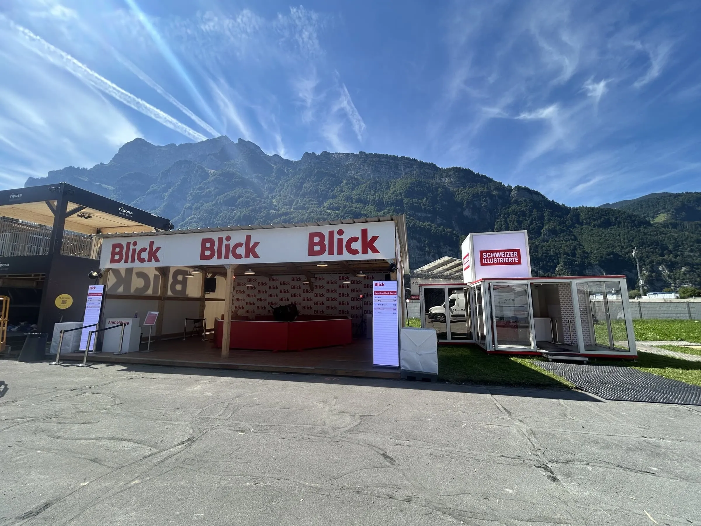 Blick wooden shelter with a rodeo arena beside Schweizer Illustrierte's glass container, against the mountains in Mollis