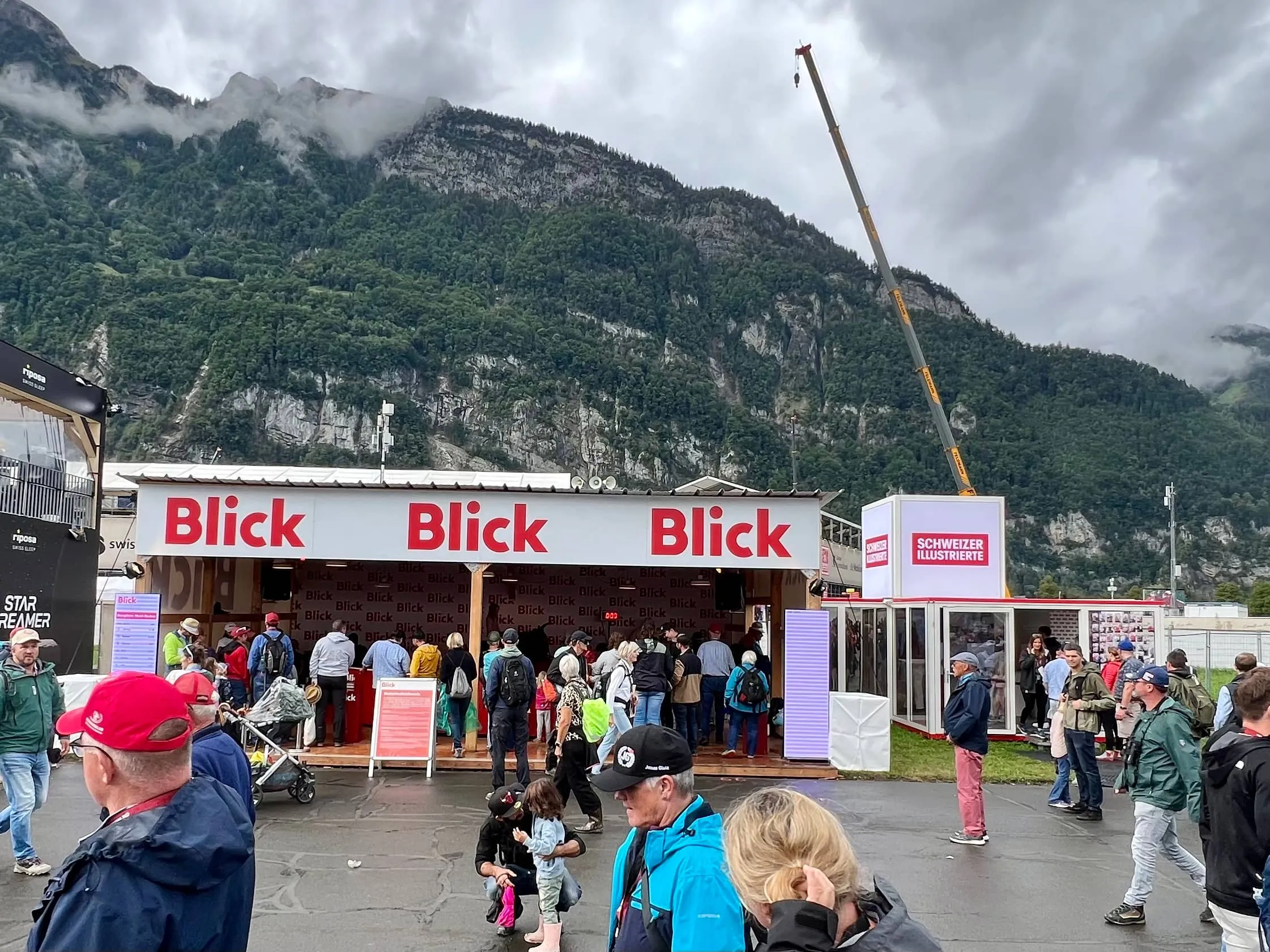 Blick-Unterstand und SI-Container mit Besuchenden, dahinter Kran und Bergkulisse des ESAF