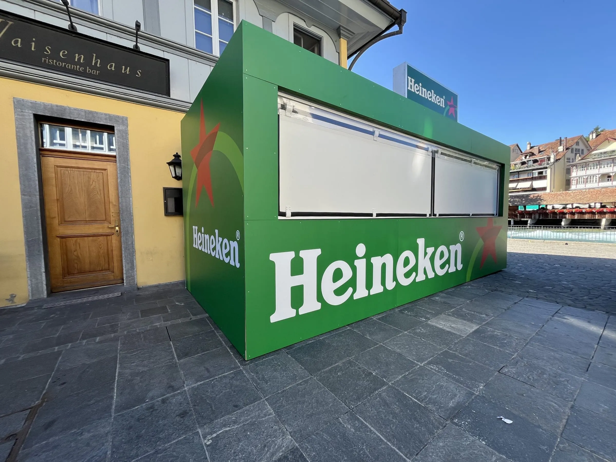 Green Heineken container with white shutters and an illuminated sign beside Restaurant Waisenhaus in Thun