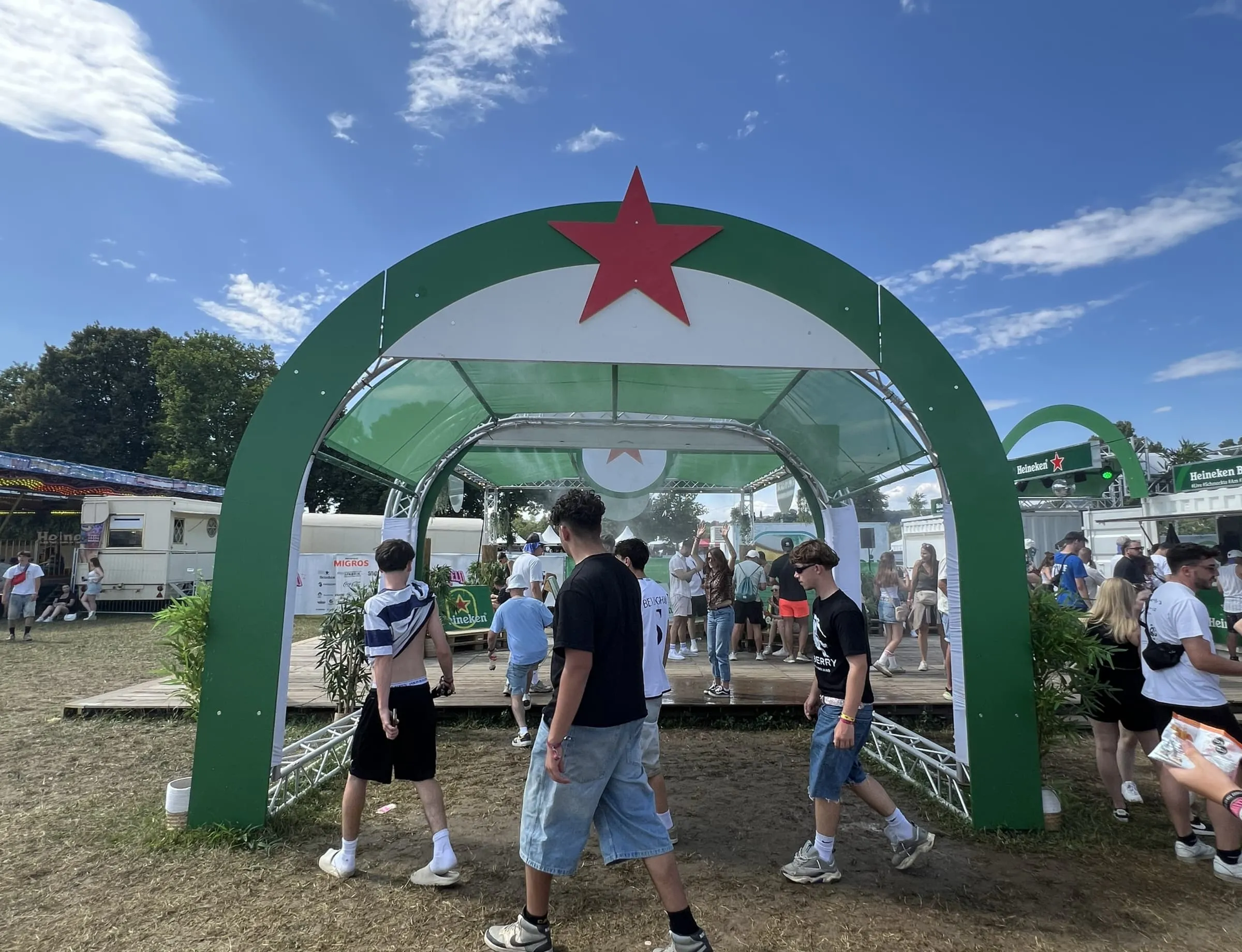 Grüner Heineken-Torbogen mit rotem Stern, junge Besucher gehen unter der Traverse zur Chillout-Area