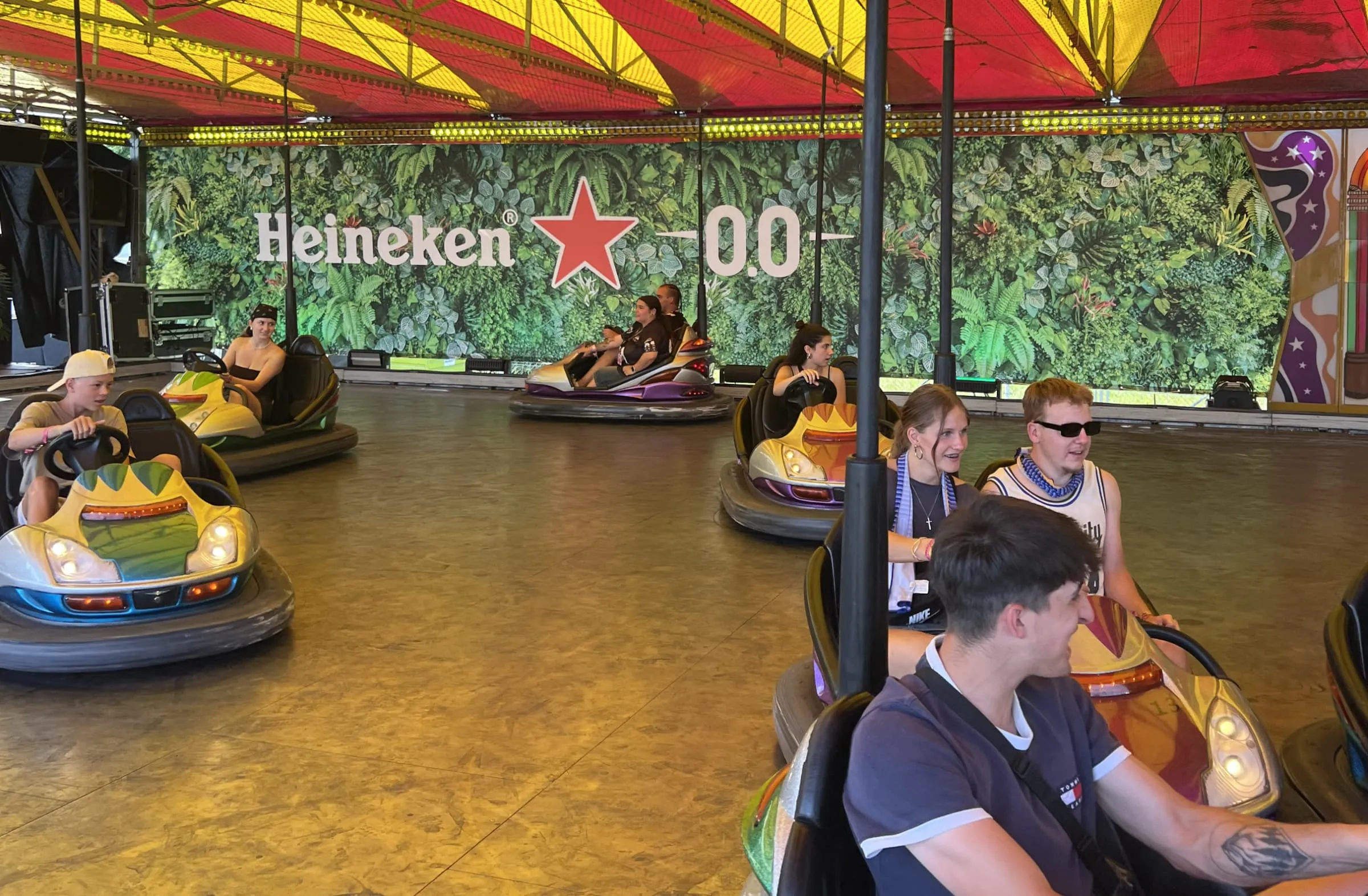 Junge Leute fahren Autoscooter vor einer grünen Pflanzenwand mit «Heineken 0.0»-Schriftzug