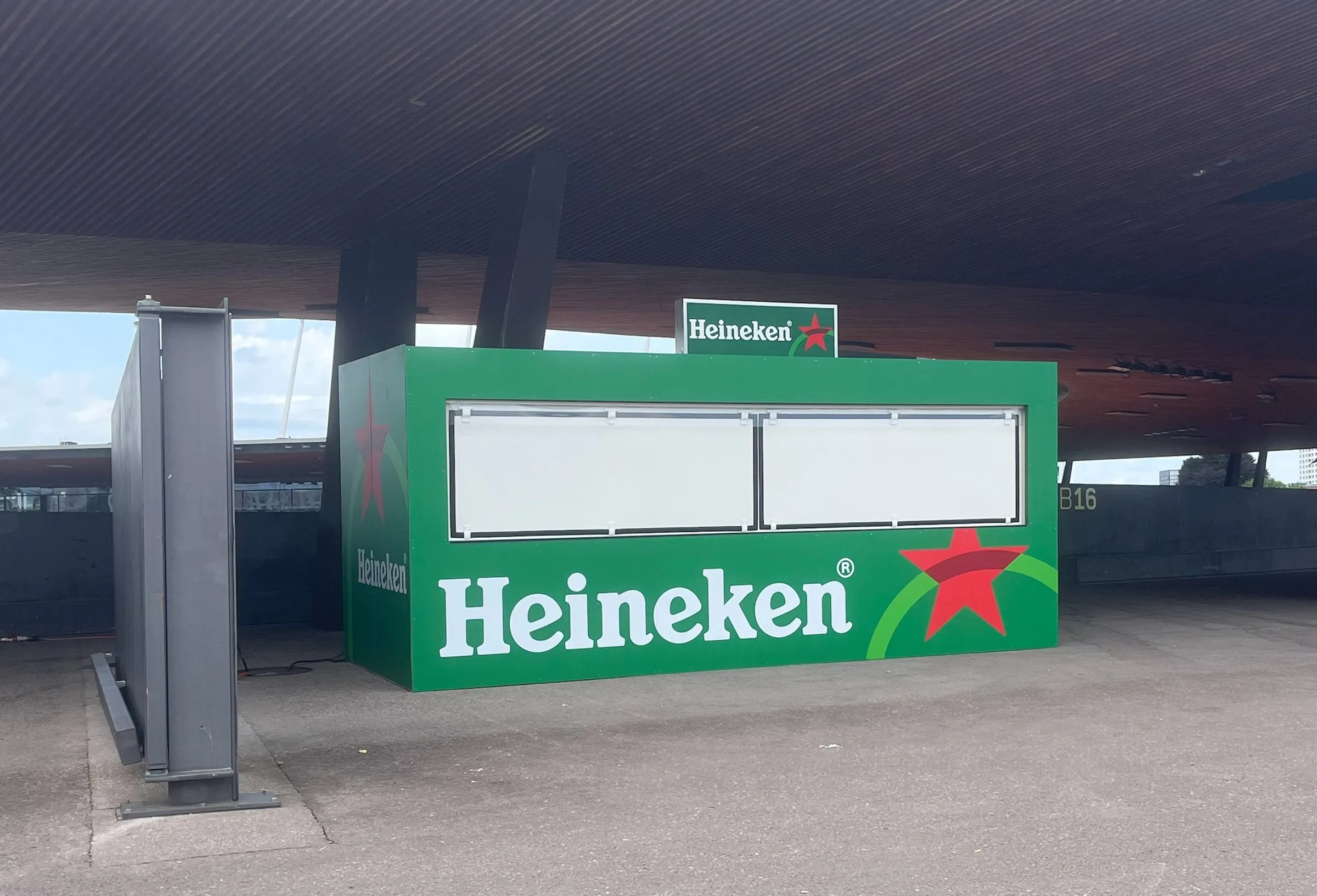 Heineken-Container mit Leuchtschild unter dem Holzdach eines Stadions in Zürich, davor eine graue Stellwand