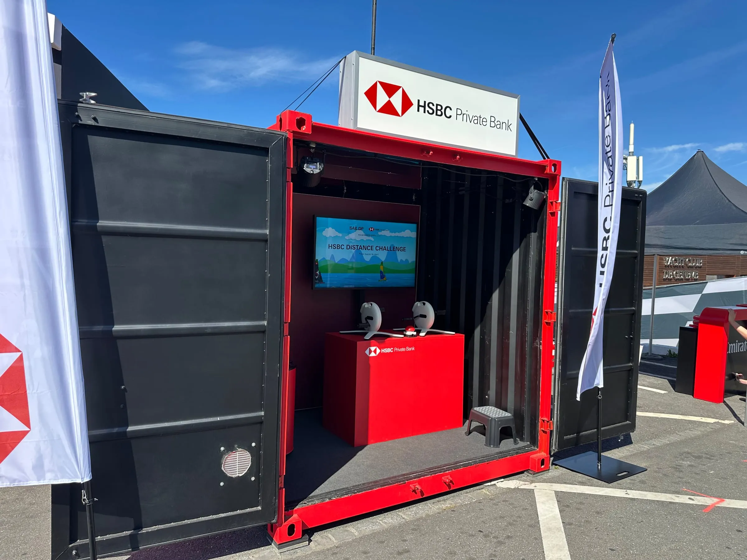Geöffneter roter Container mit Screen «HSBC Distance Challenge», Pedalen und Buzzer auf rotem Podest