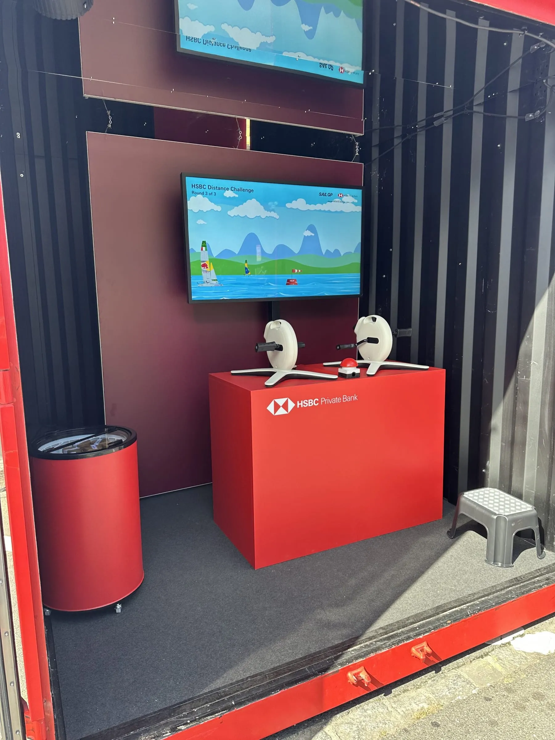 Innenraum des Containers mit Spielscreen, zwei weissen Pedaltrainern, rotem Buzzer und Eisbox