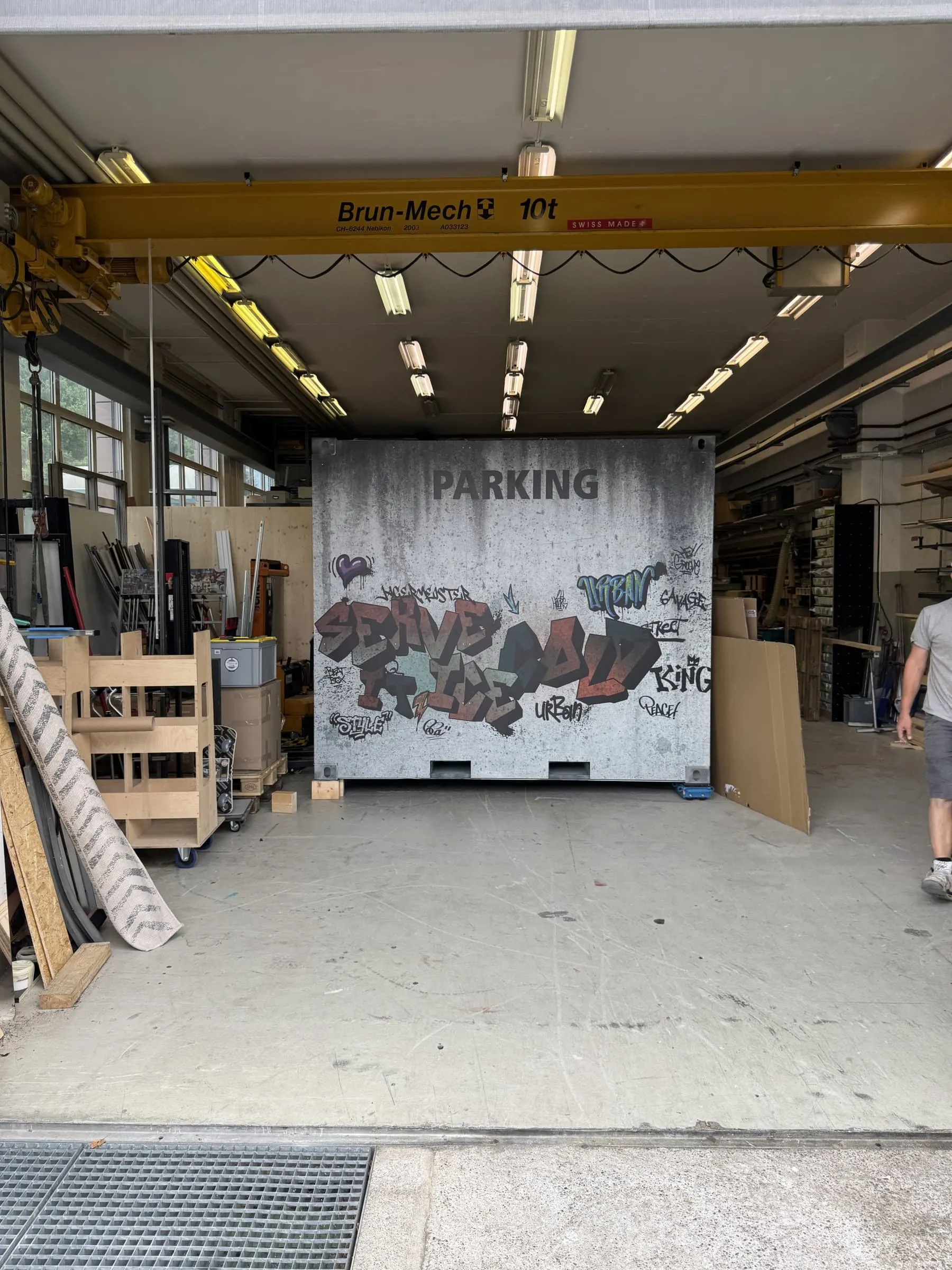 Container in der Werkstatt mit «Parking»-Aufschrift und Graffiti «Serve it Ice Cold» im Betonlook