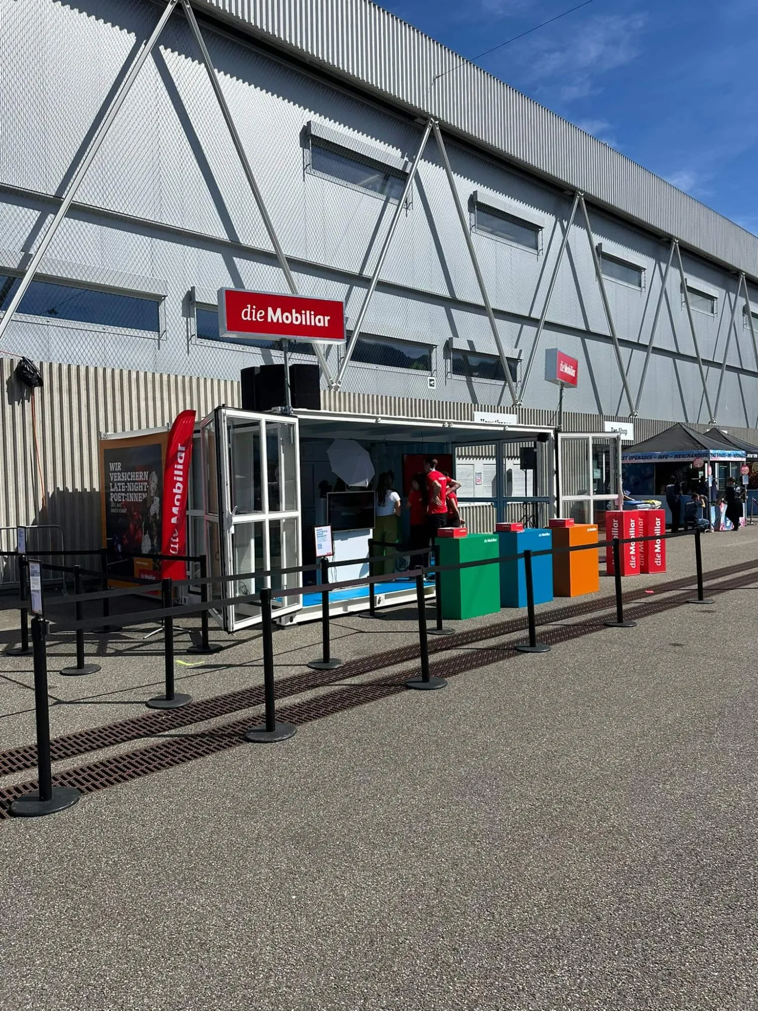 Open container by day with a red Mobiliar flag, coloured cubes and promoters inside