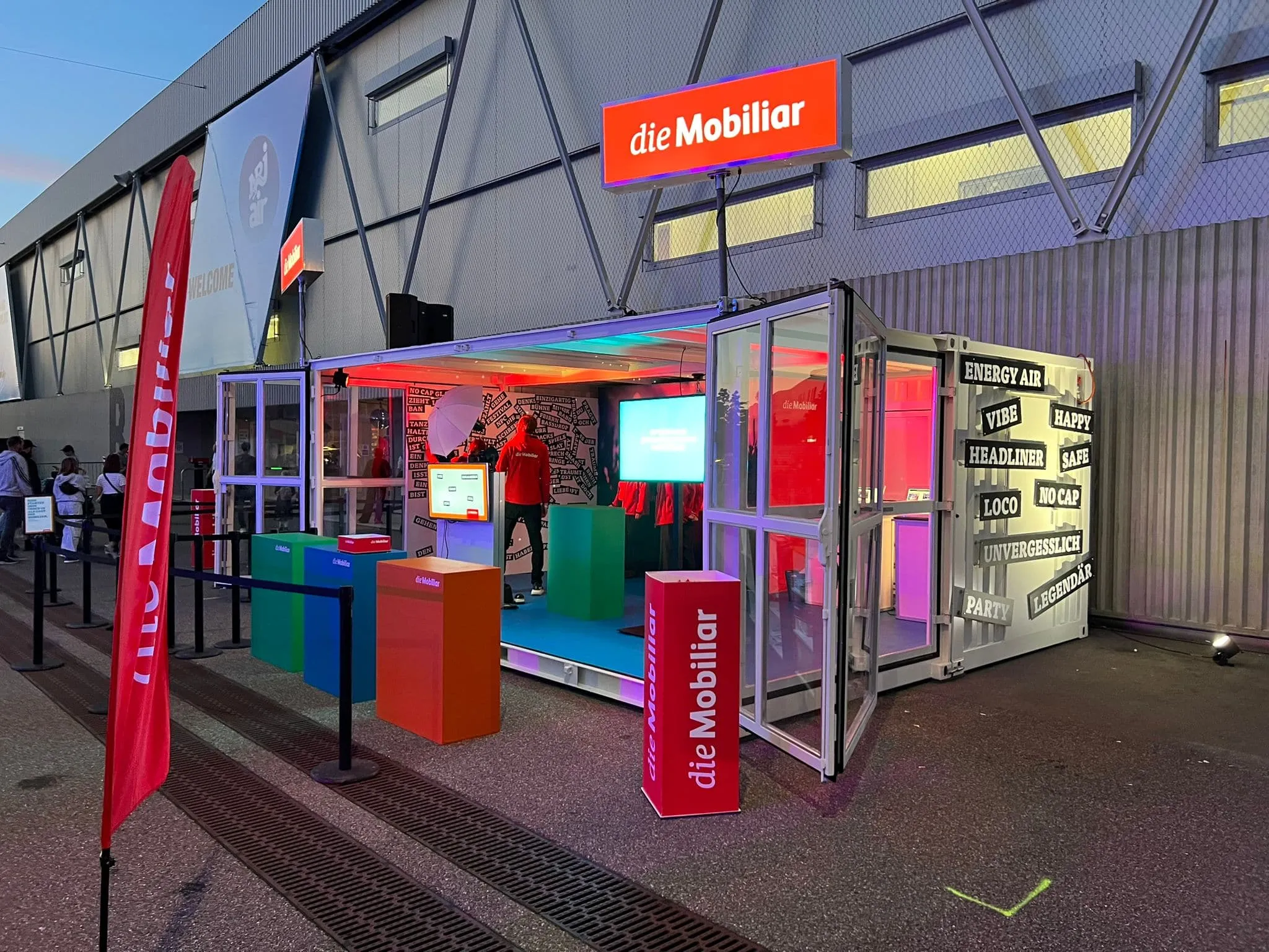 Container at dusk, lit from inside, with words such as «Energy Air», «Vibe» and «Headliner» on the outer wall