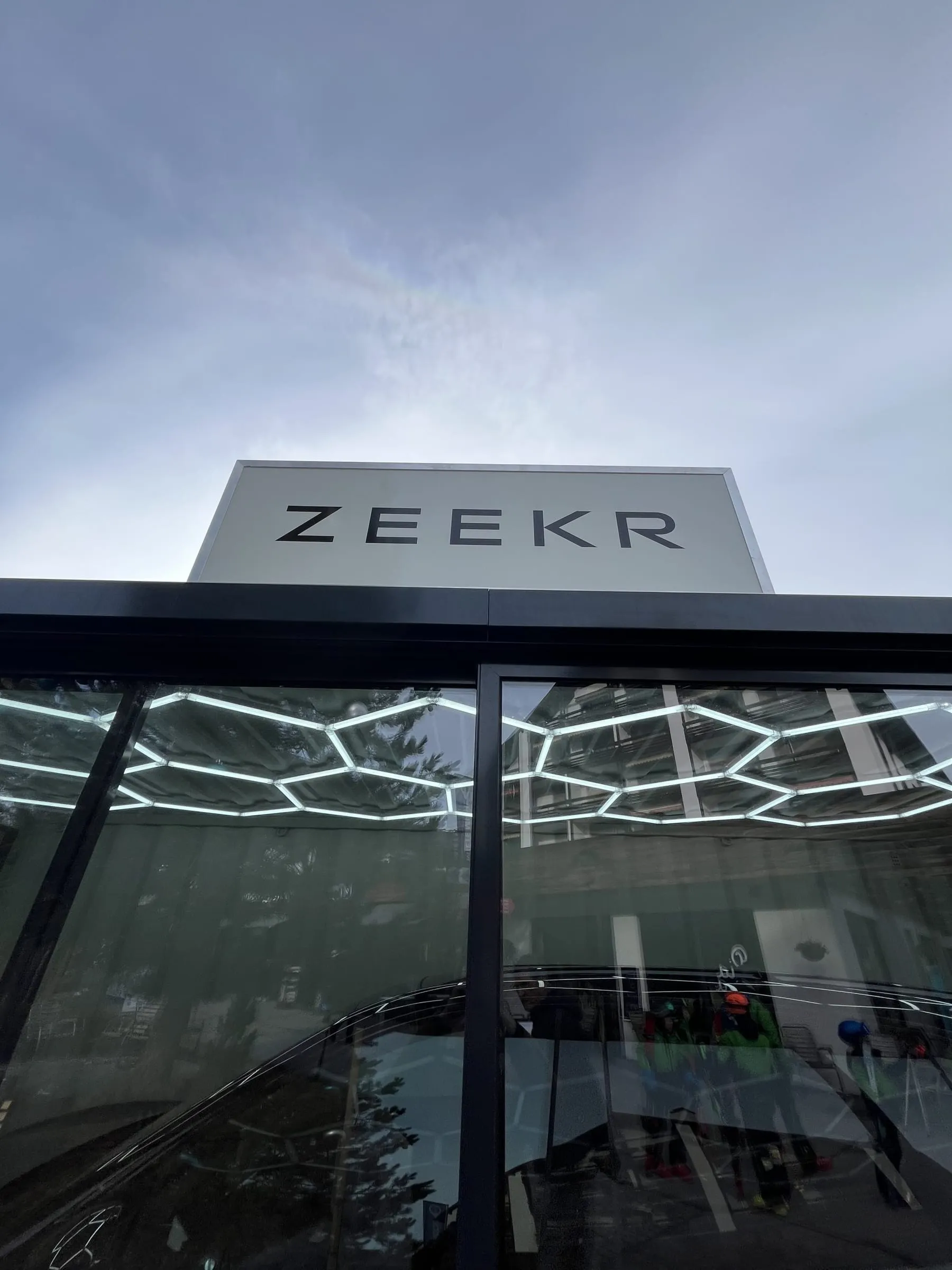 Blick nach oben auf das weisse Zeekr-Leuchtschild über der Glasfront, innen wabenförmige LED-Deckenleuchten