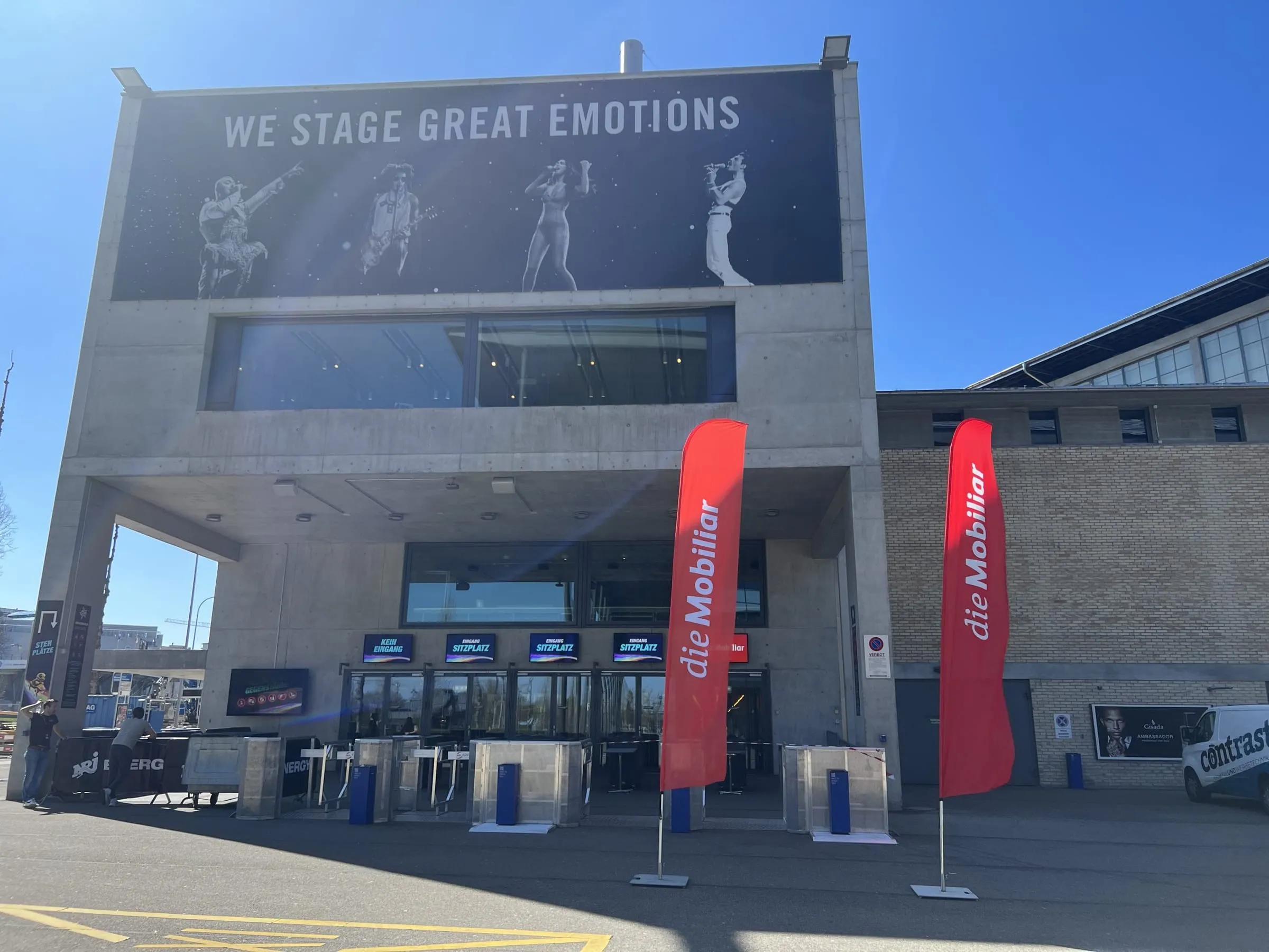 Entrance of the Hallenstadion Zürich with two red Mobiliar beach flags in front of the lettering «We stage great emotions»