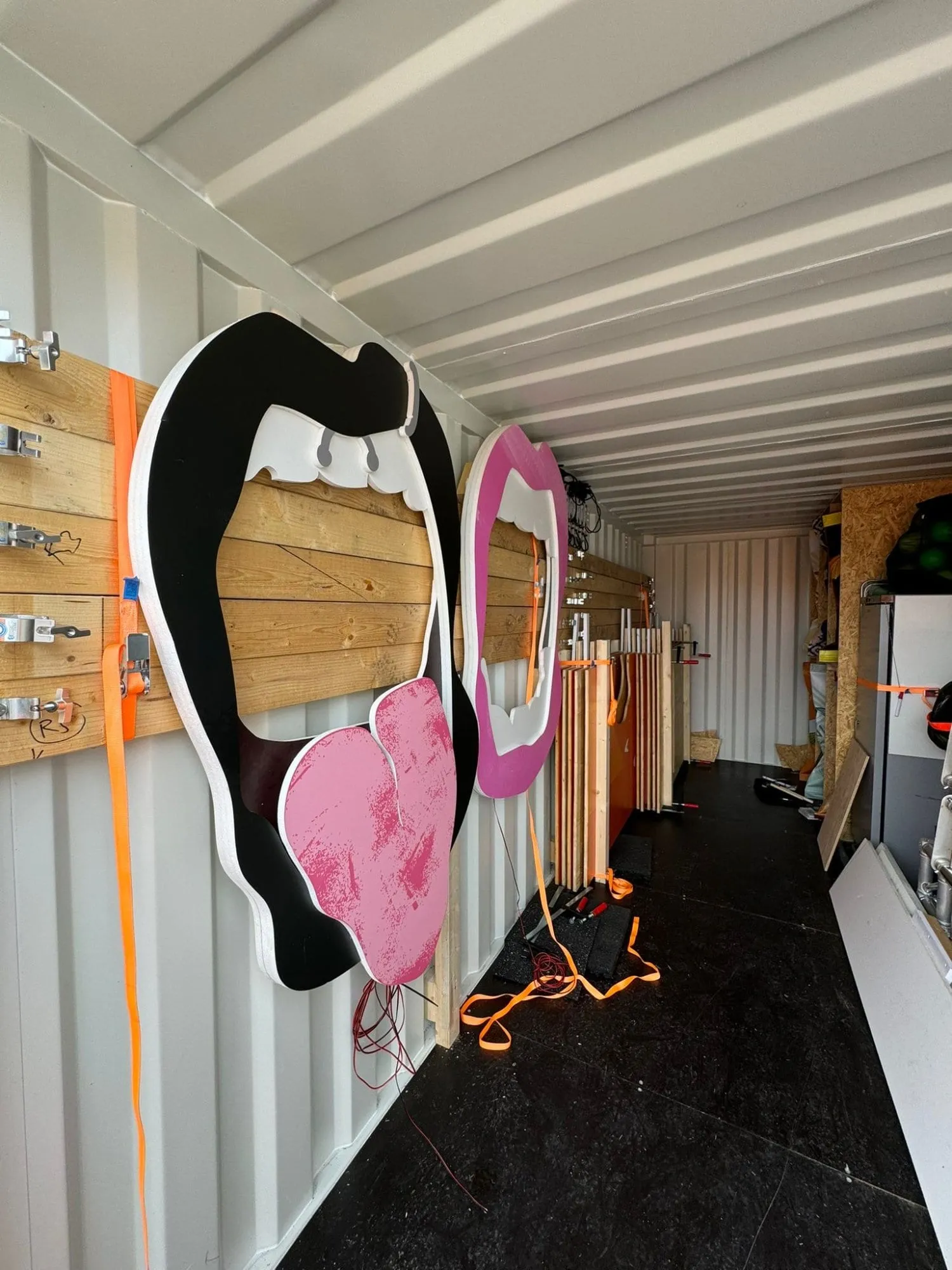 Zwei ausgeschnittene Mund-Elemente in Schwarz-Pink und Pink lagern verzurrt im Container