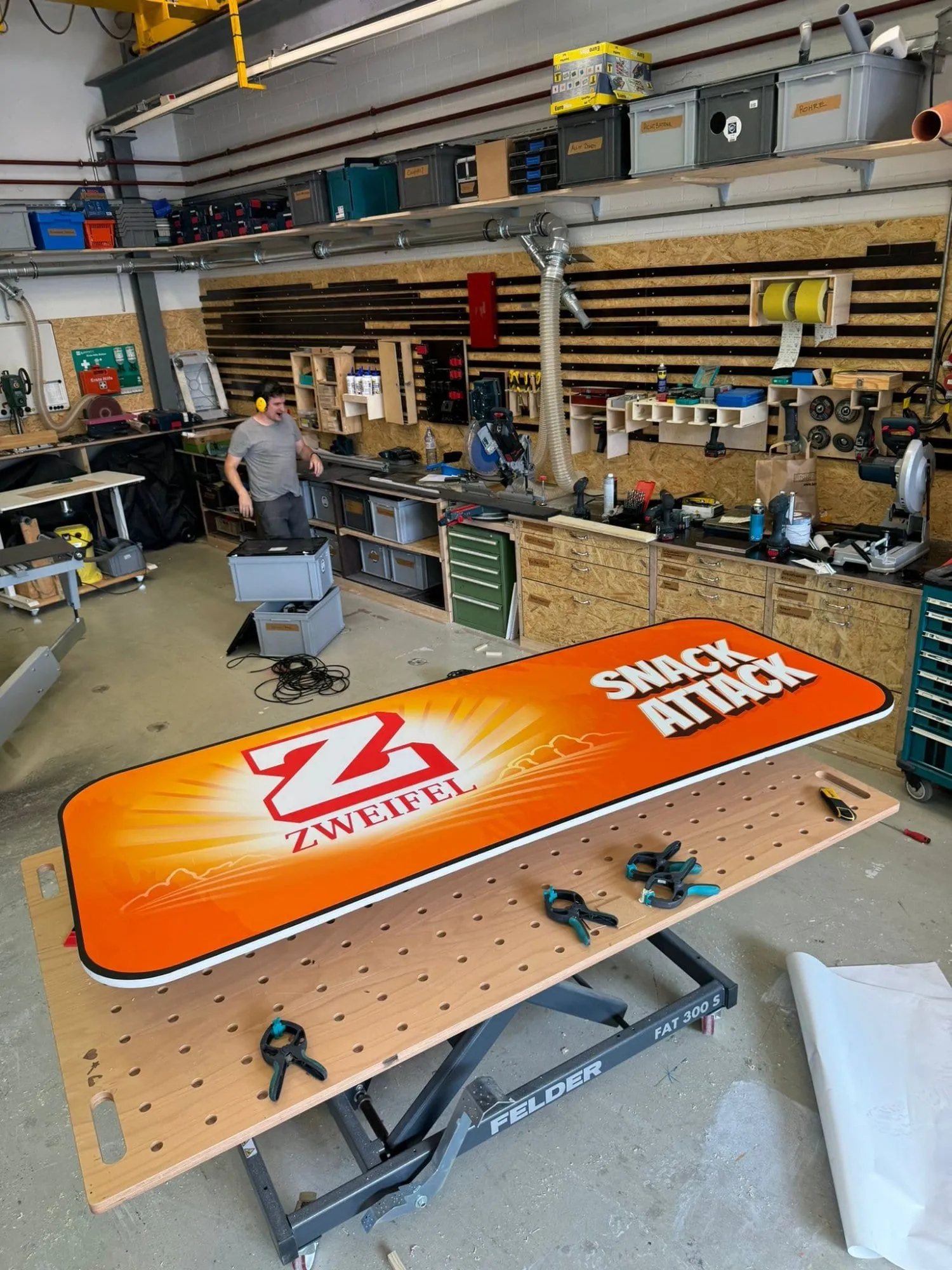 Oranges Leuchtschild mit Zweifel-Logo und Schriftzug Snack Attack auf dem Werktisch in der Werkstatt