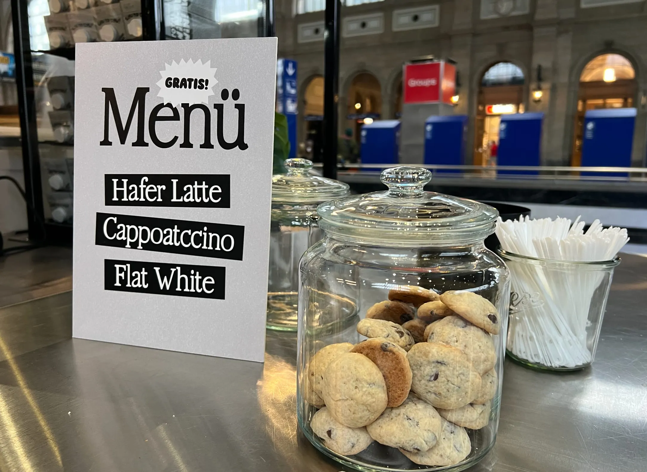 Glas mit Hafercookies und Menükarte «Gratis Menü: Hafer Latte, Cappoatccino, Flat White» auf der Theke