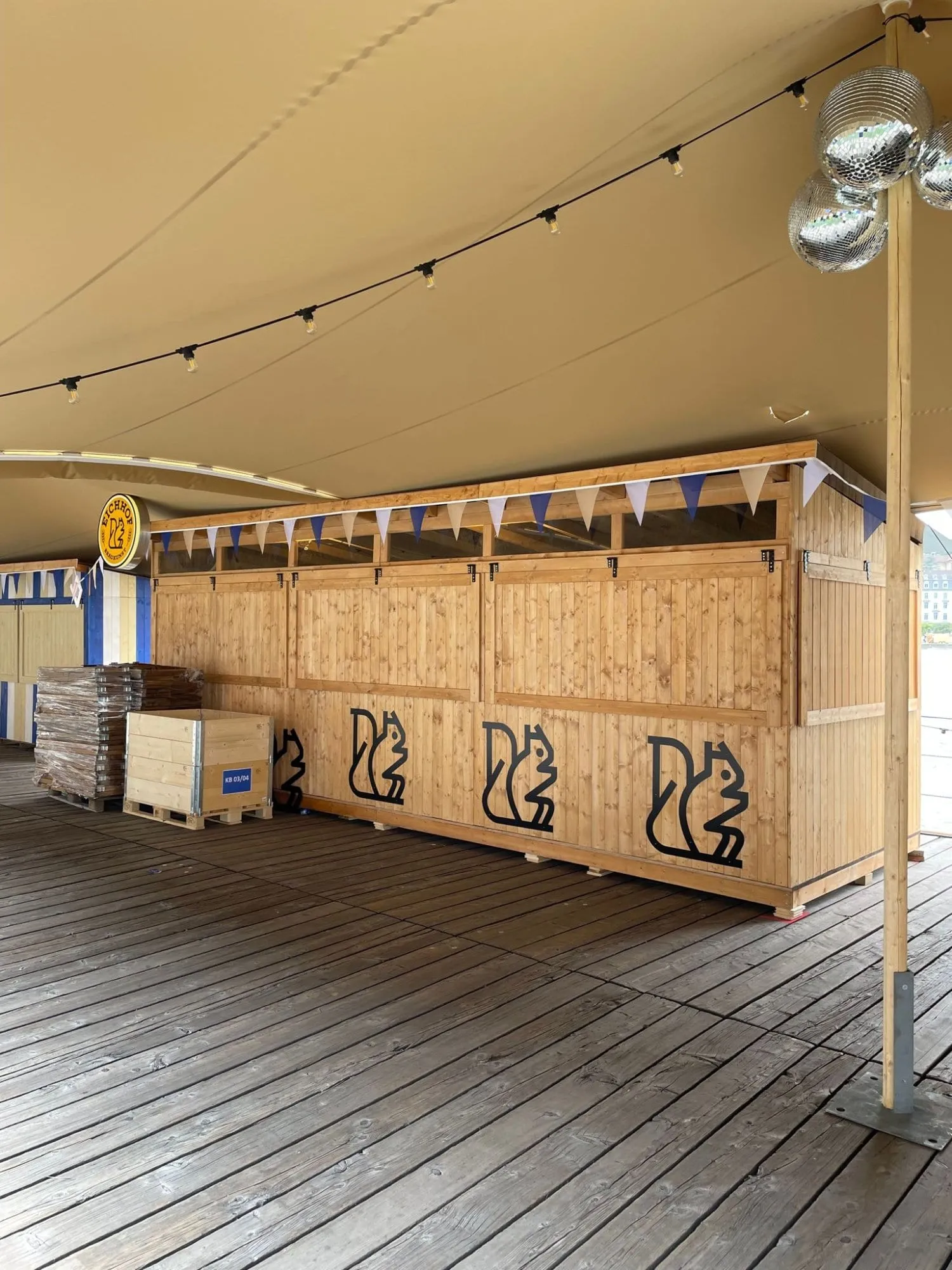 Holzbar mit schwarzen Eichhörnchen-Logos, Wimpeln, Eichhof-Leuchtschild und Discokugeln unter dem Zeltdach