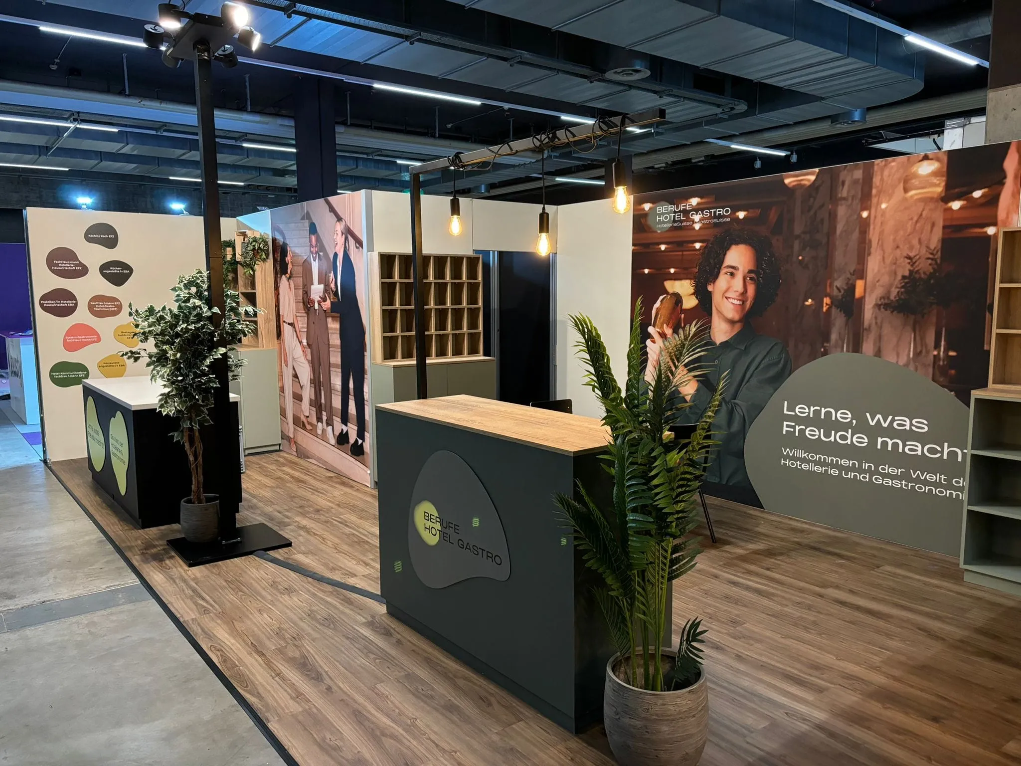 Messestand von der Seite mit Theke mit Logo Berufe Hotel Gastro, Fotowand mit Barkeeper und Tafel mit Berufsbezeichnungen