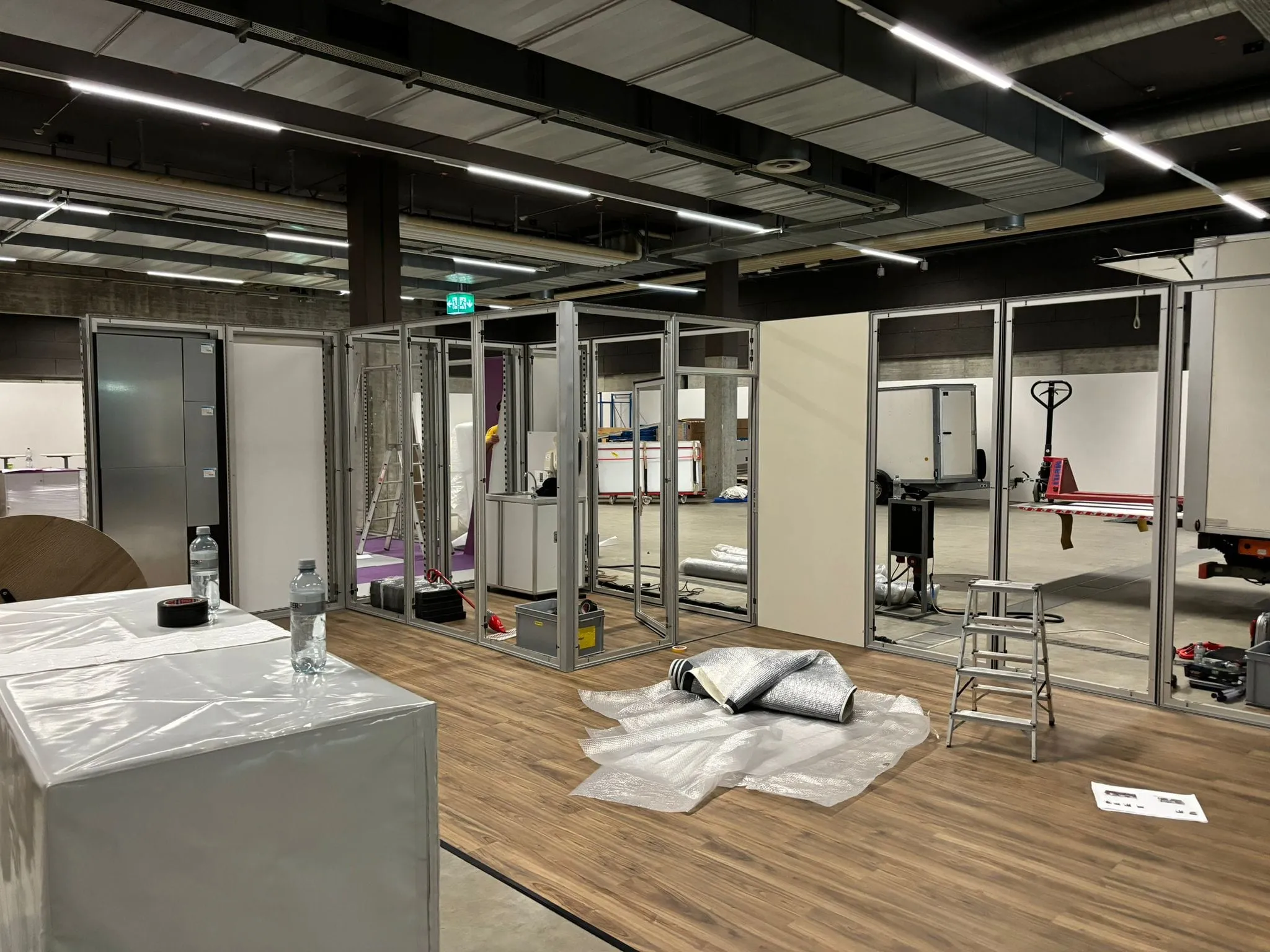 Aluminium-Rahmenwände im Aufbau, Leiter, Luftpolsterfolie und Anhänger in der Messehalle