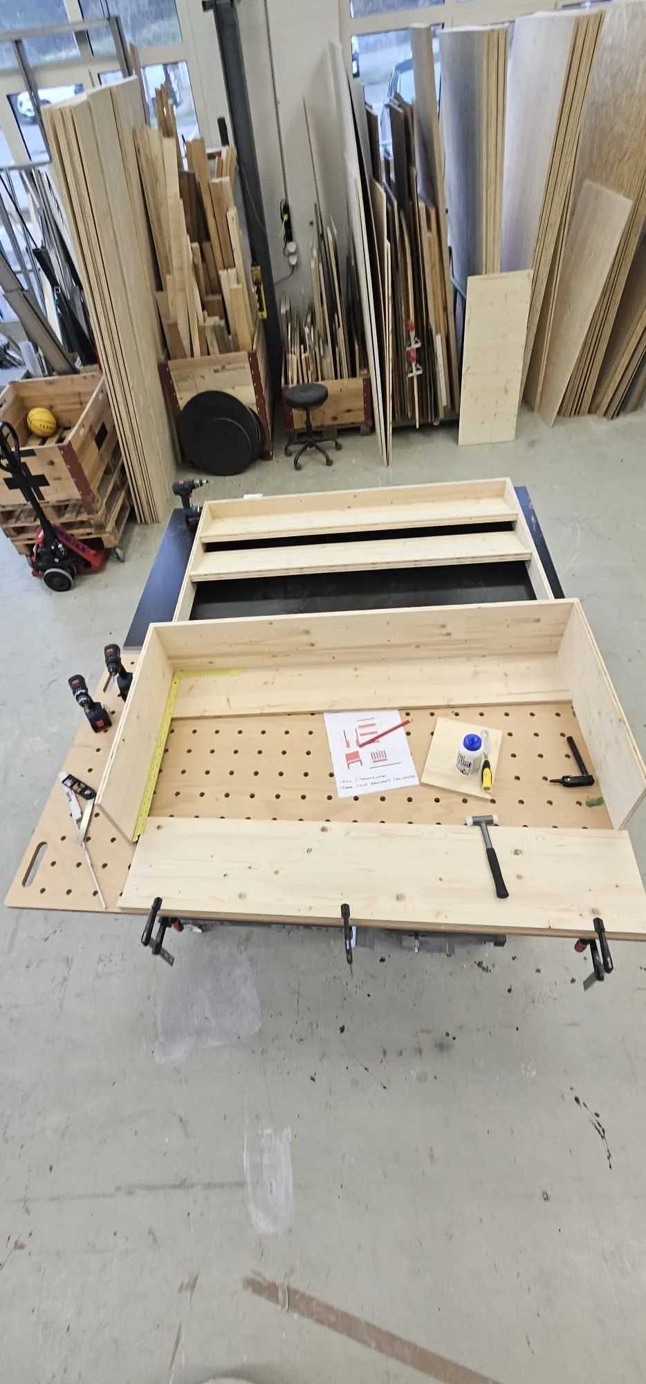 Rohbau des Regals aus hellem Holz auf dem Werktisch in der Werkstatt, mit Plan, Leim und Werkzeug
