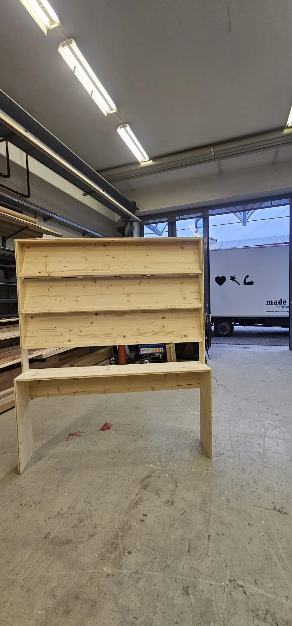 Unlackiertes Holzregal mit drei Tablaren und Ablage in der Werkstatt, im Hintergrund der made-Lieferwagen