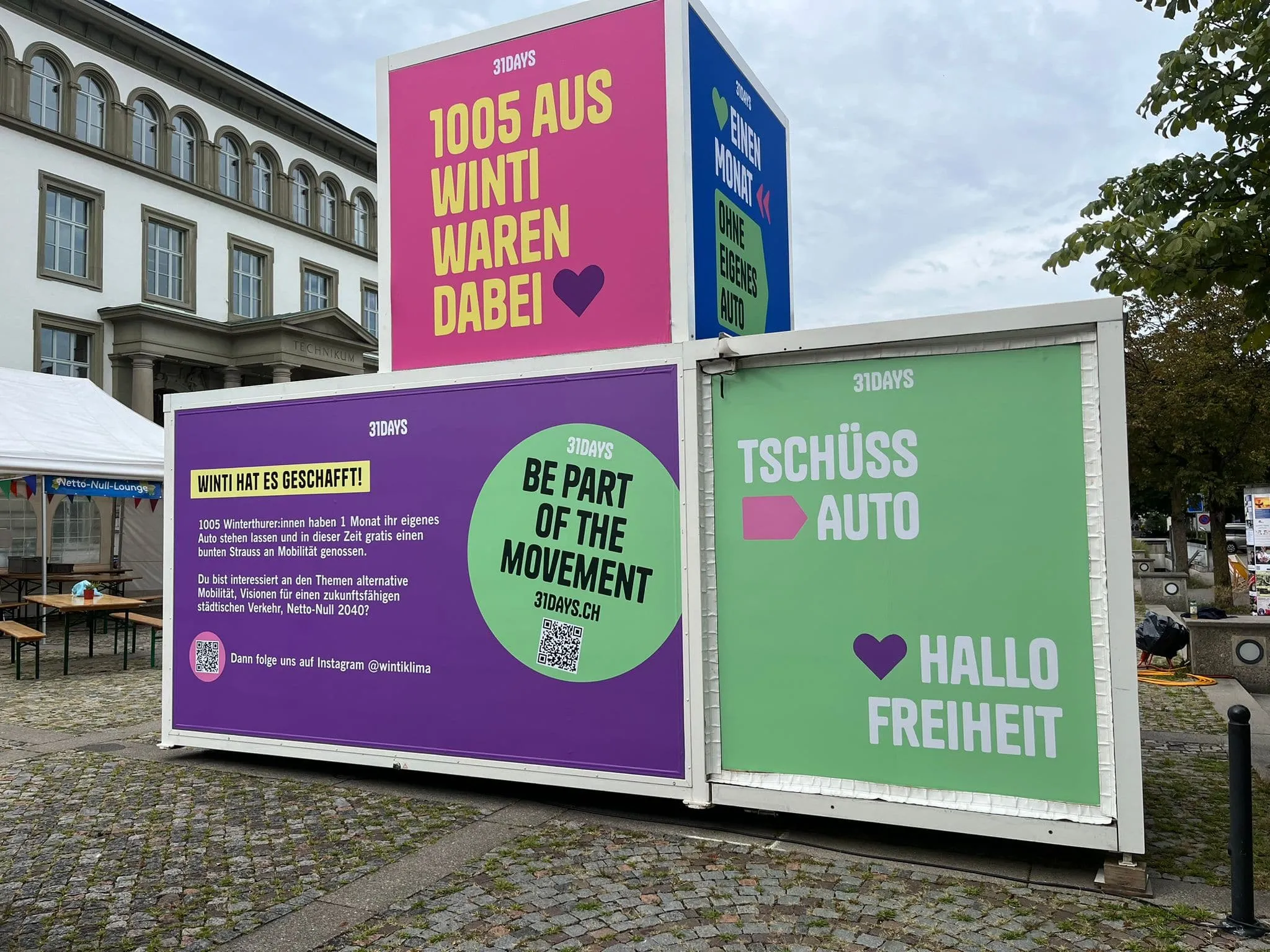 Rückseite des Promocubes mit violetten, grünen und pinken 31DAYS-Flächen vor dem Technikum-Gebäude