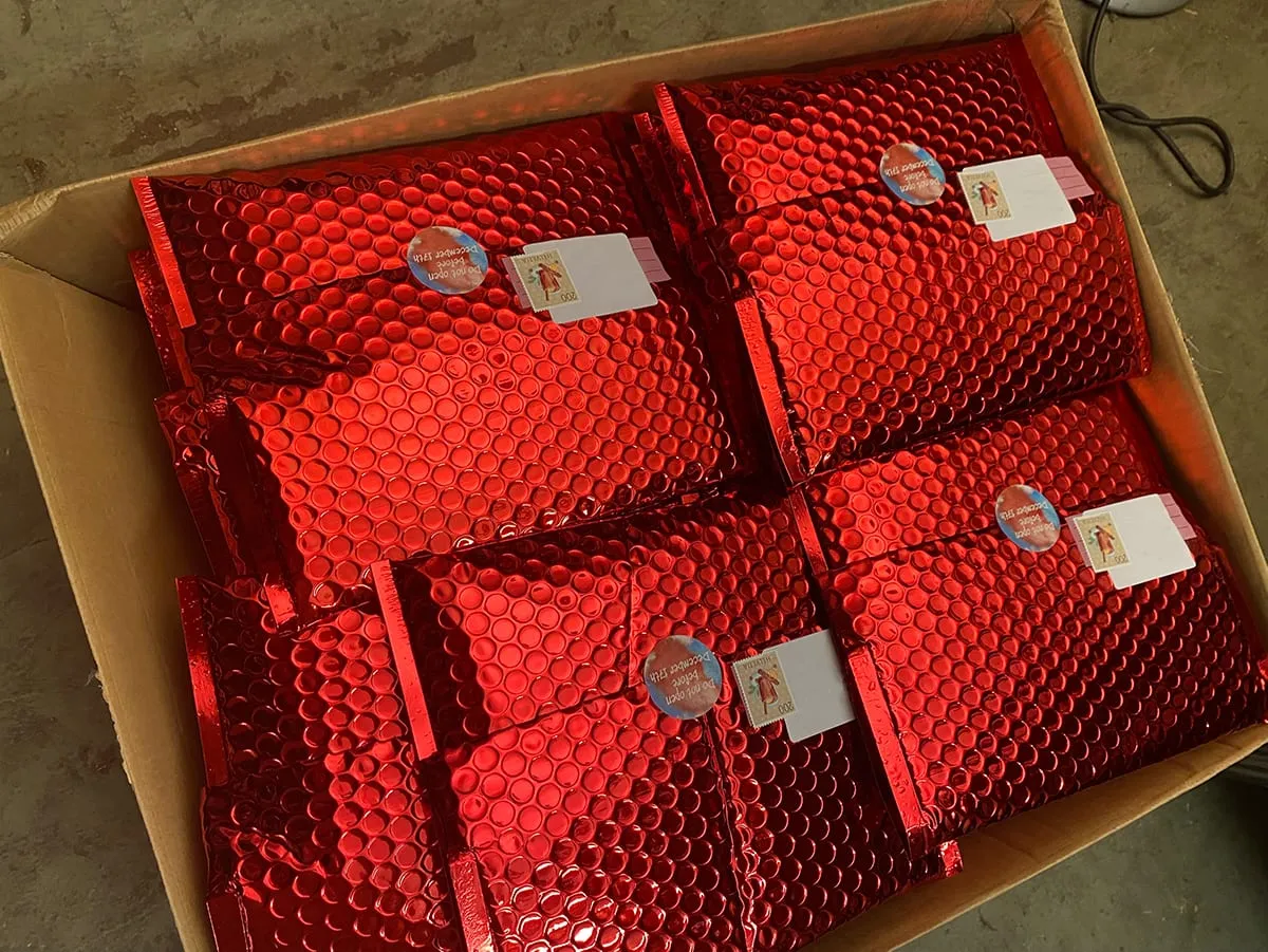 Karton voller roter, glänzender Luftpolster-Versandtaschen mit Adressetiketten und Briefmarken