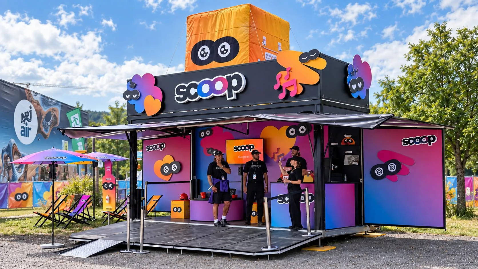 Black scoop container with a colourful logo, eye emojis and an orange cube on the roof, three promoters on the stage and deckchairs alongside