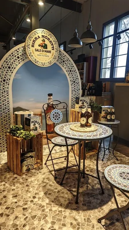 Torbogen mit Sale-di-Mare-Logo im Laden, davor Mosaiktisch mit Flaschen, Holzkisten mit Bierkartons und Efeu