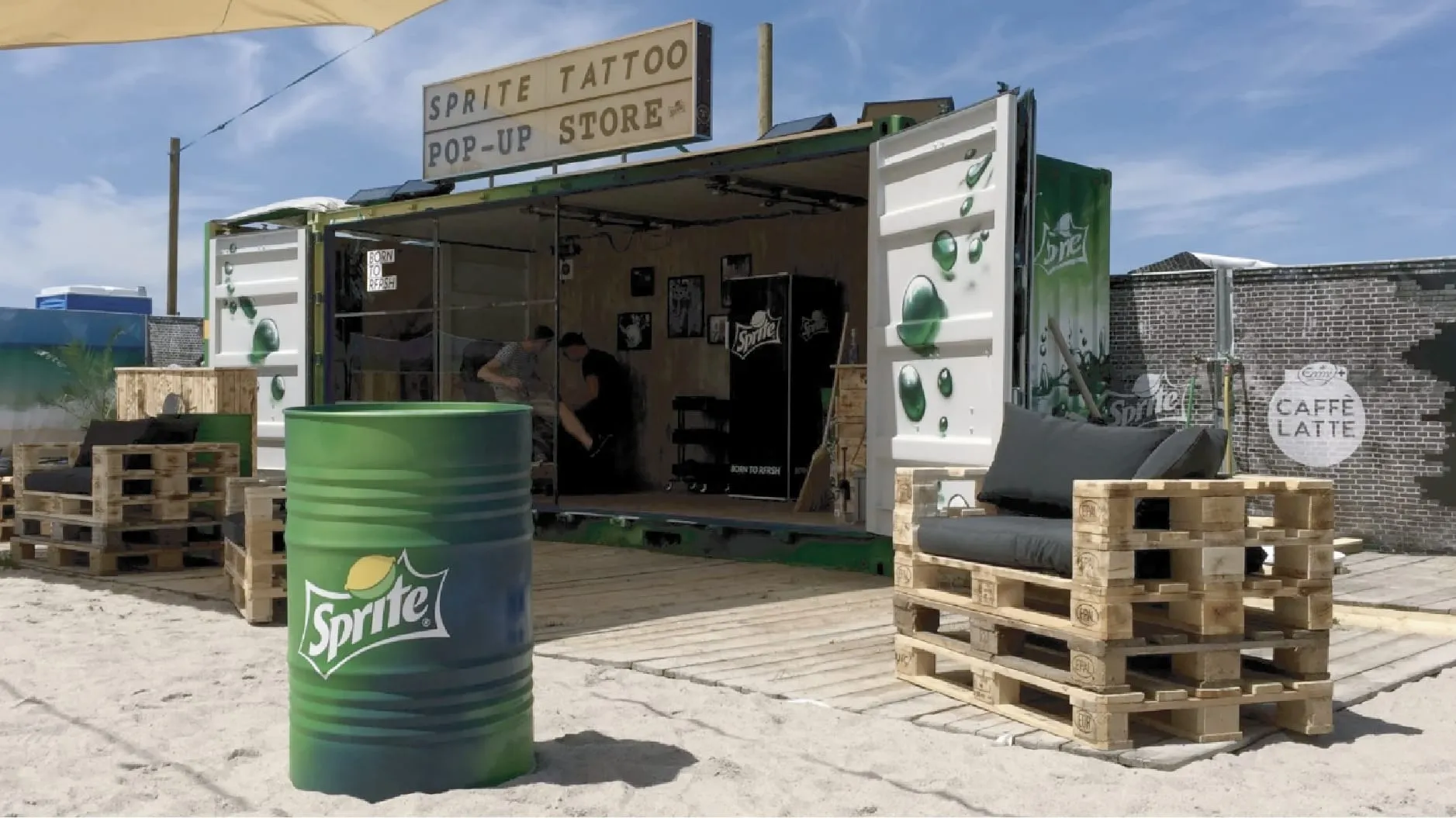 Sprite Tattoo pop-up store in an opened container on sand, with pallet sofas and a green barrel