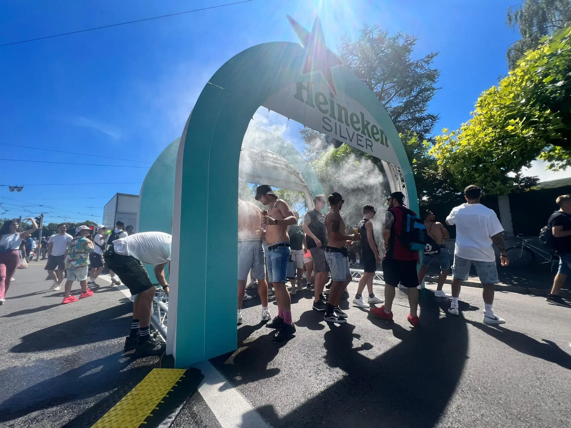 Turquoise Heineken Silver misting arch with a red star, with festival visitors underneath in the spray at Street Parade