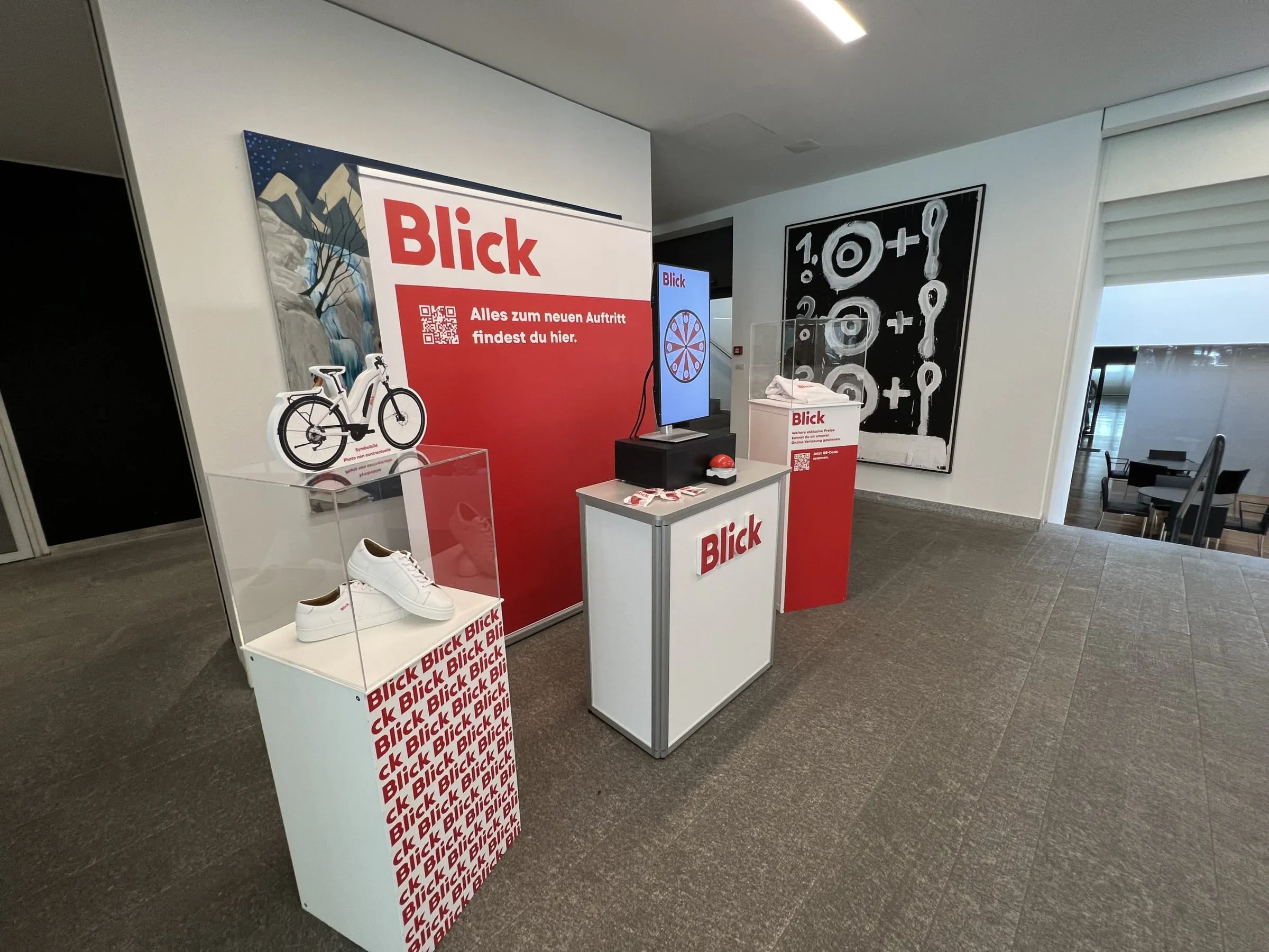 Blick stand in a foyer with a red back wall, a digital Glücksrad on screen and display cases with sneakers