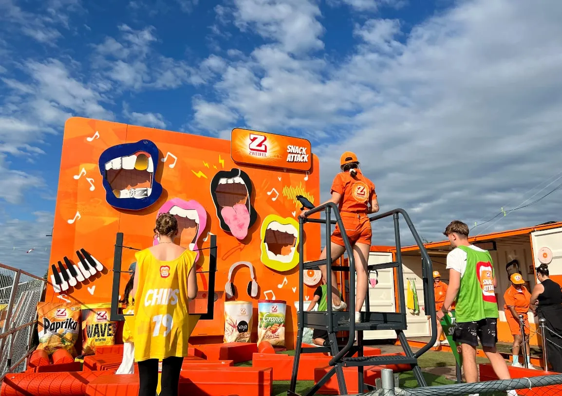 Orange Snack Attack wall with four oversized mouths, players in team bibs and a promoter on the platform