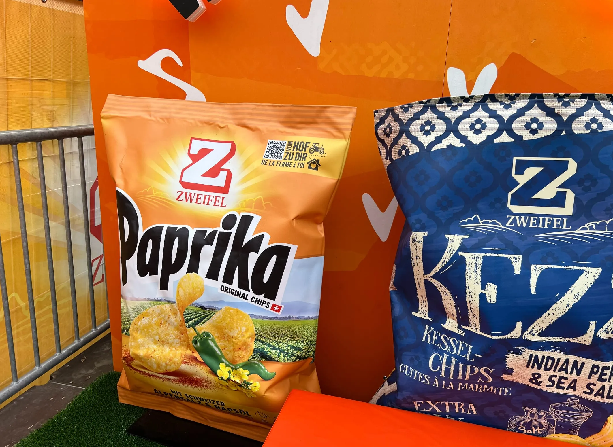 Übergrosse Zweifel-Chipstüten Paprika und Kezz vor der orangen Spielwand