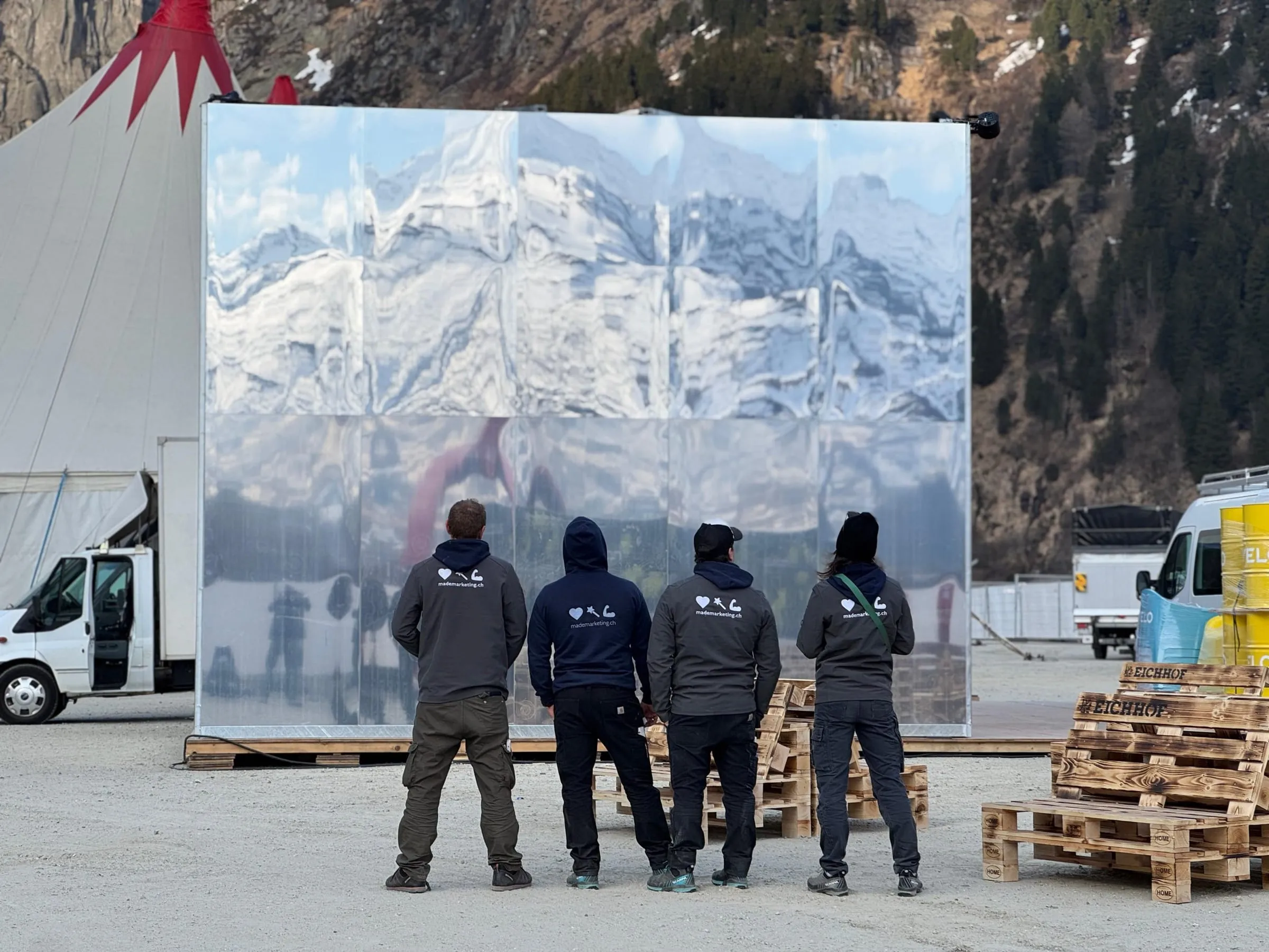 Four made team members seen from behind in front of the Velo mirror cube, reflecting snow-covered mountains