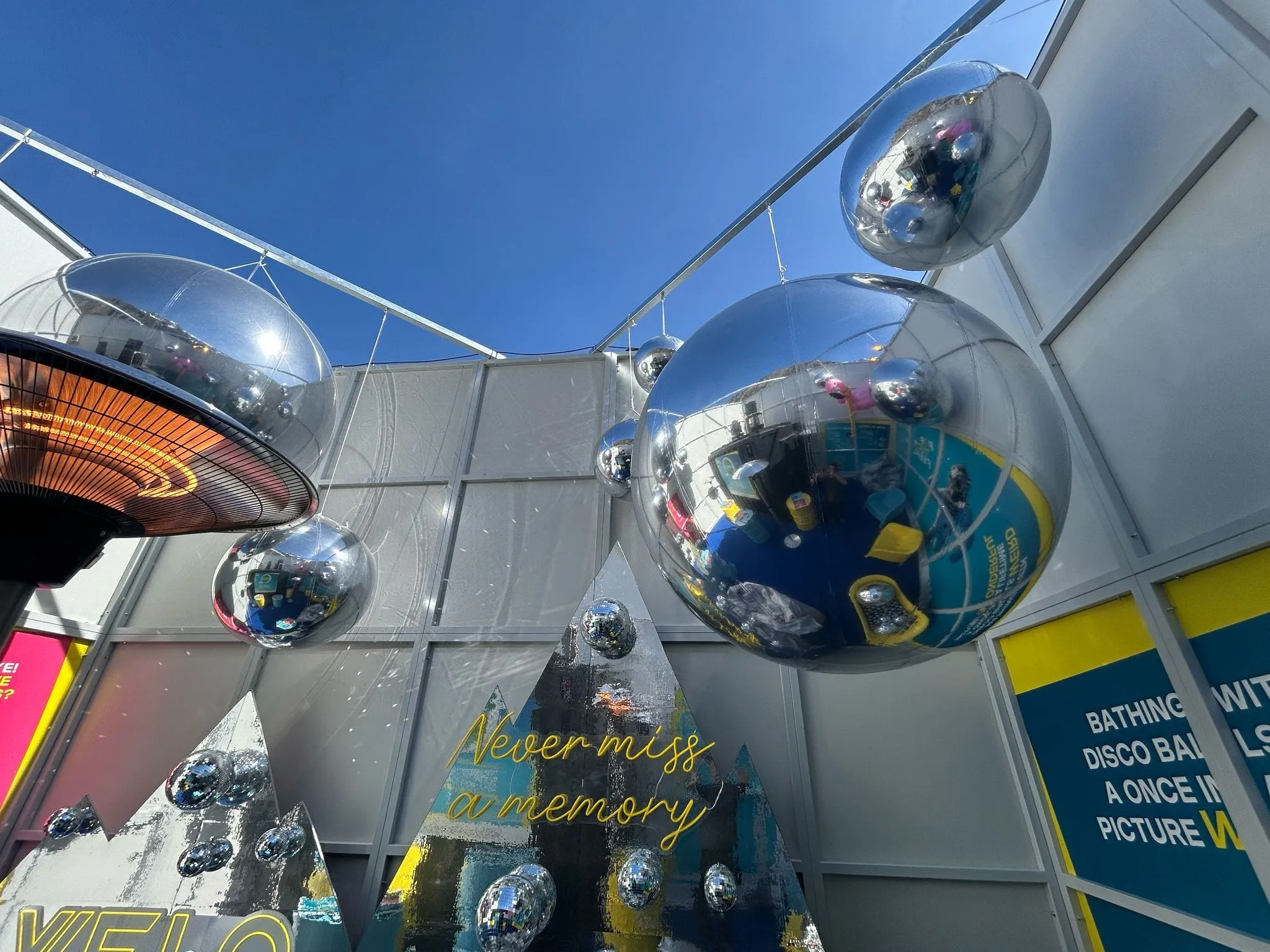 Silberne Spiegelballons über dem offenen Innenhof, darunter Spiegelpyramiden mit Neonschrift «Never miss a memory»