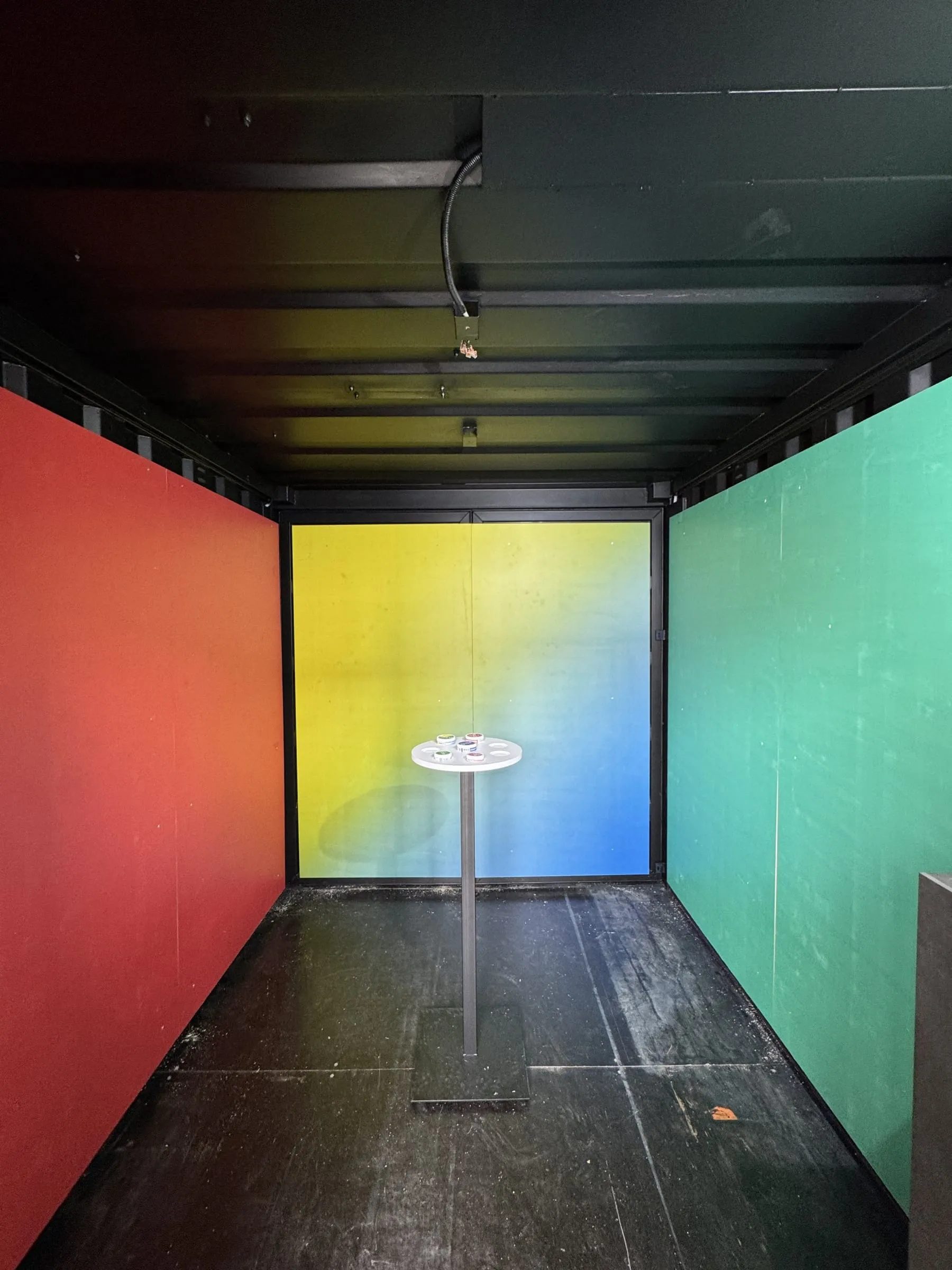 Containerinnenraum mit roter, gelb-blau verlaufender und grüner Wand, in der Mitte das runde Interaktions-Board