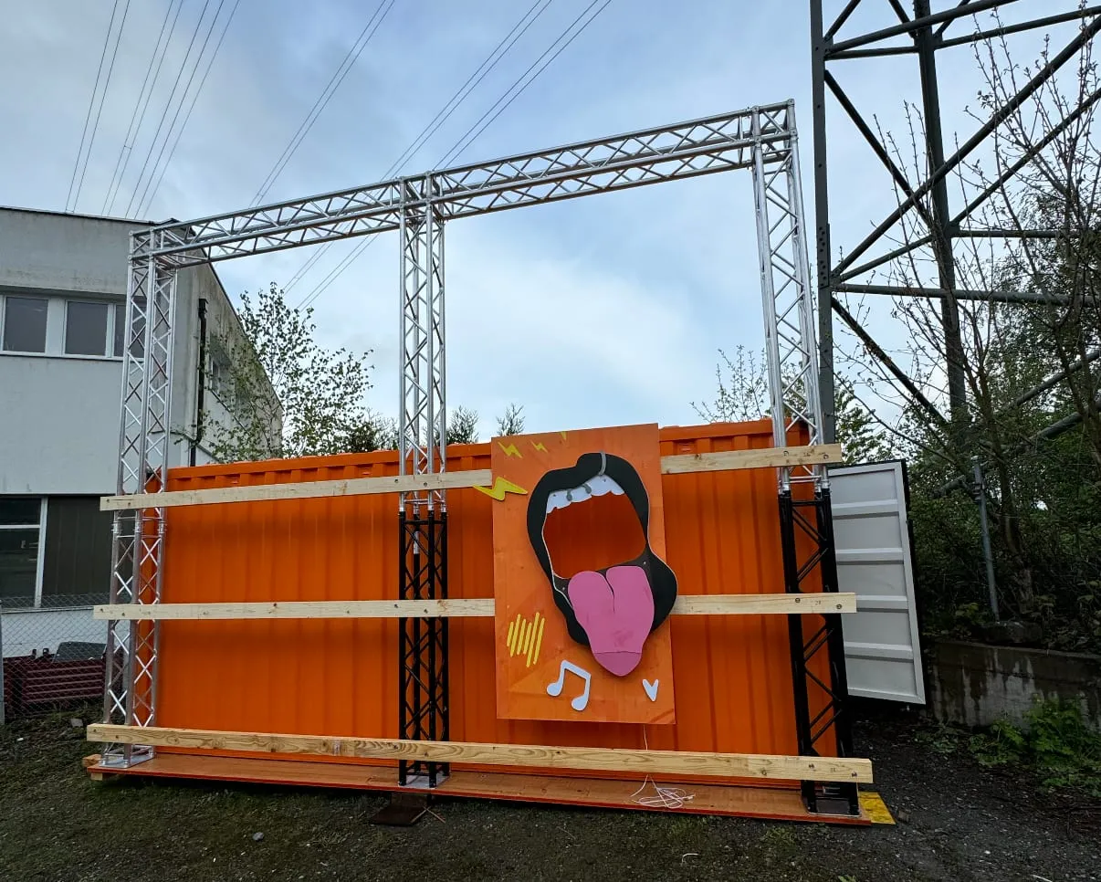 Testaufbau vor der Werkstatt: oranger Container mit Traversen und einem ersten Mund-Element aus Holz