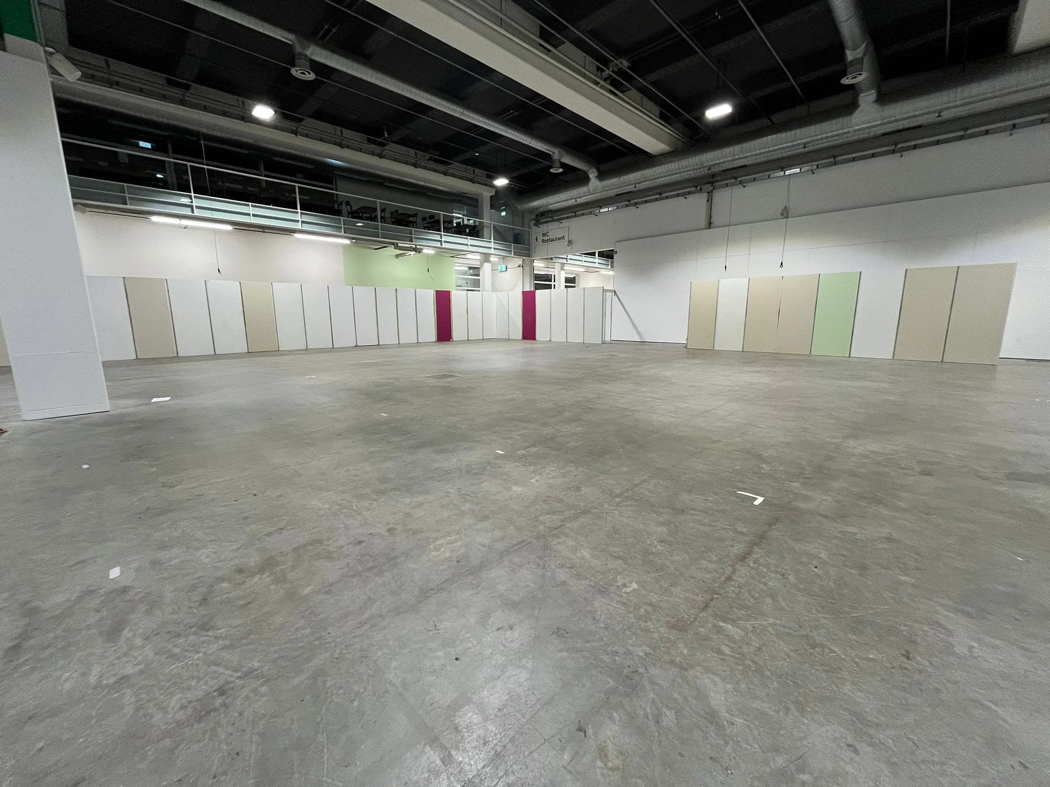 Leere Messehalle mit Betonboden und beigen, weissen und pinken Wandpaneelen vor dem Aufbau